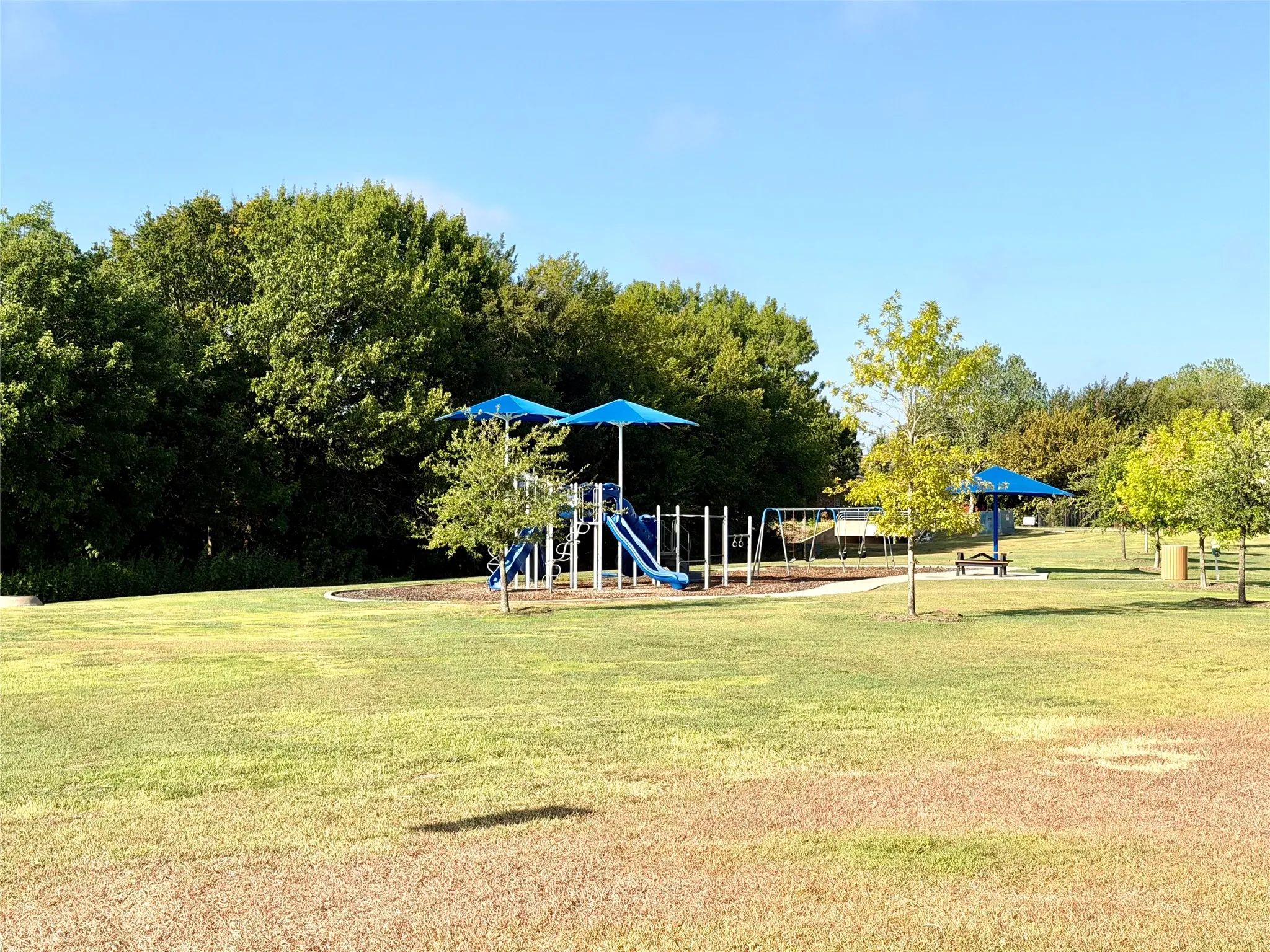 Expansive green space featuring a playground with blue shade structures, swings, and a slide