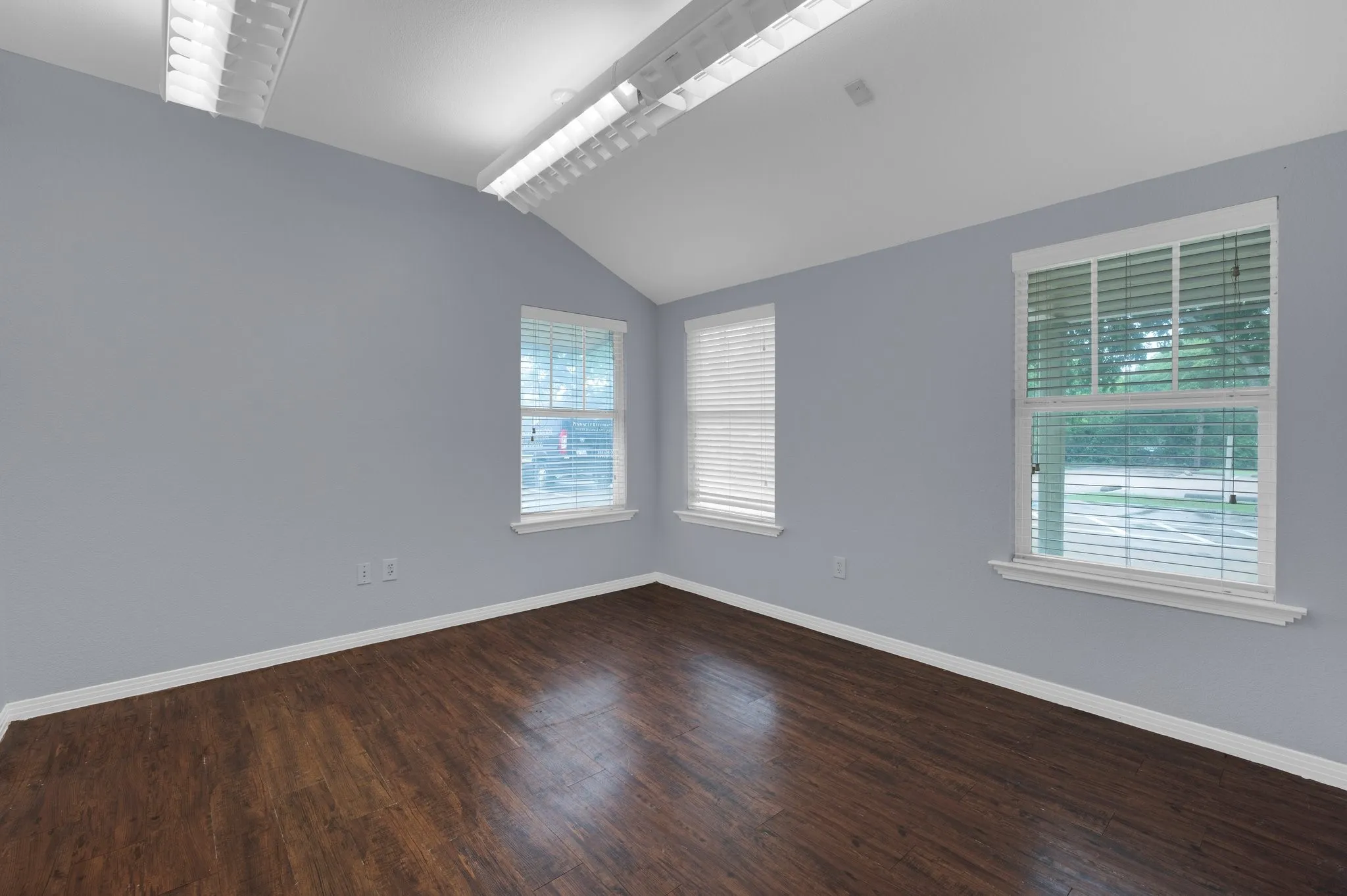 Vaulted ceiling with exposed beams, wood-finish flooring, and multiple windows with blinds