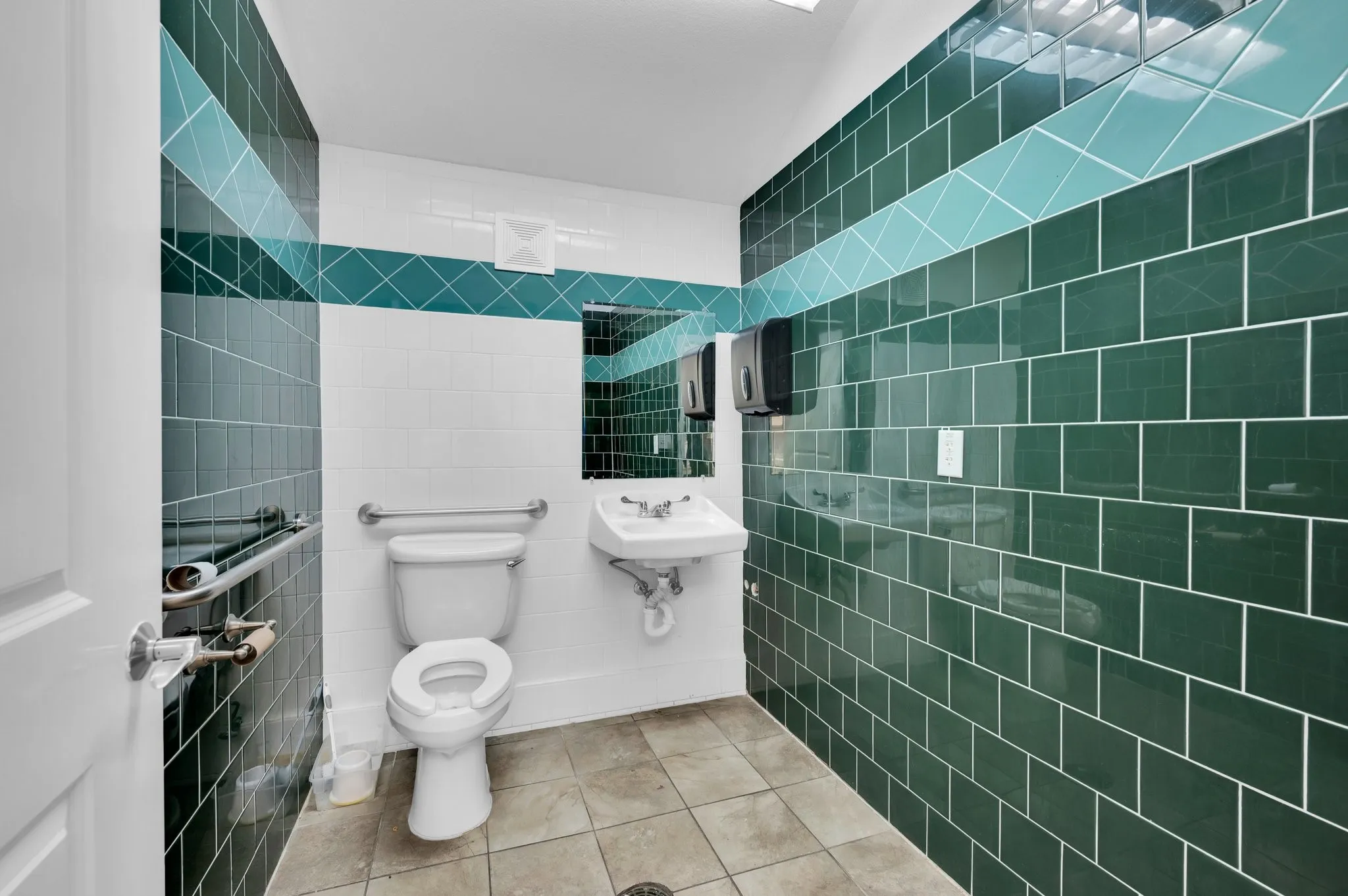 Restroom featuring dark green subway tile walls with a contrasting teal accent band, white painted walls, a wall-mounted sink, and a white toilet