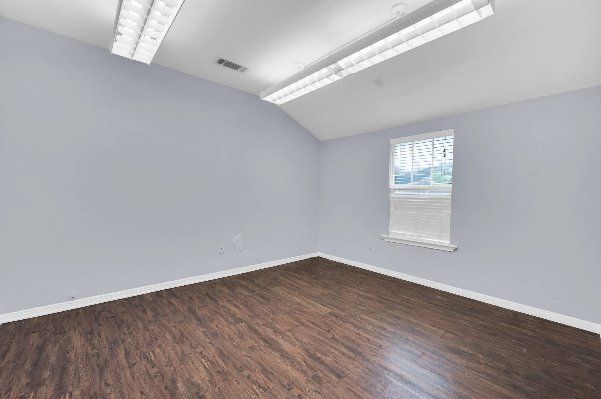 Spacious interior featuring wood-finish flooring, light blue walls, and a vaulted ceiling