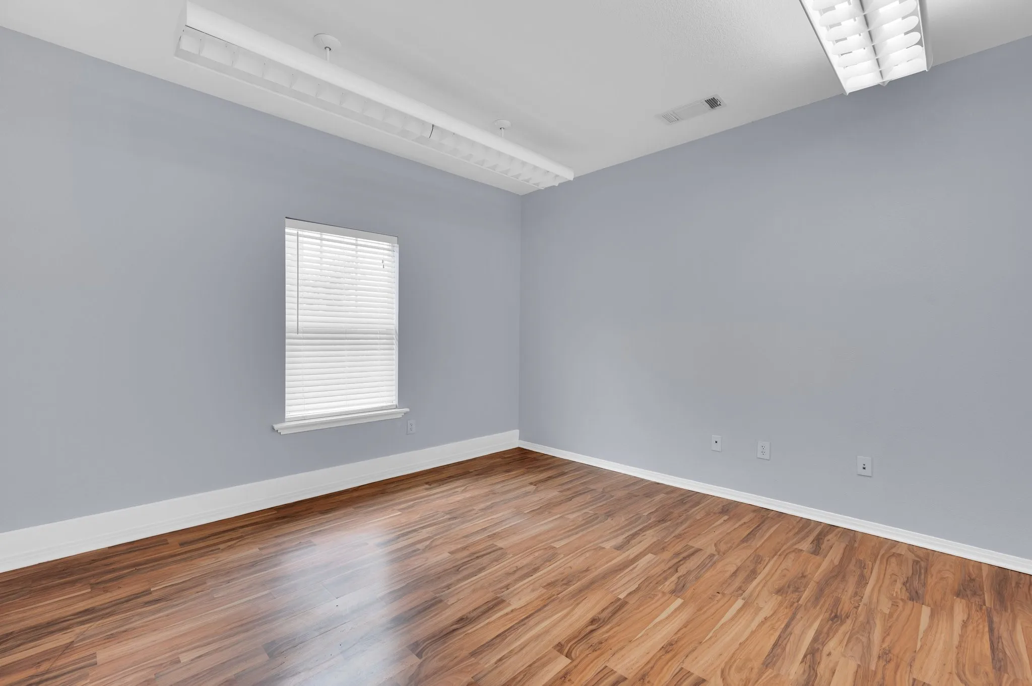 Bright interior space featuring wood-finish flooring, a window with blinds, and contemporary overhead lighting