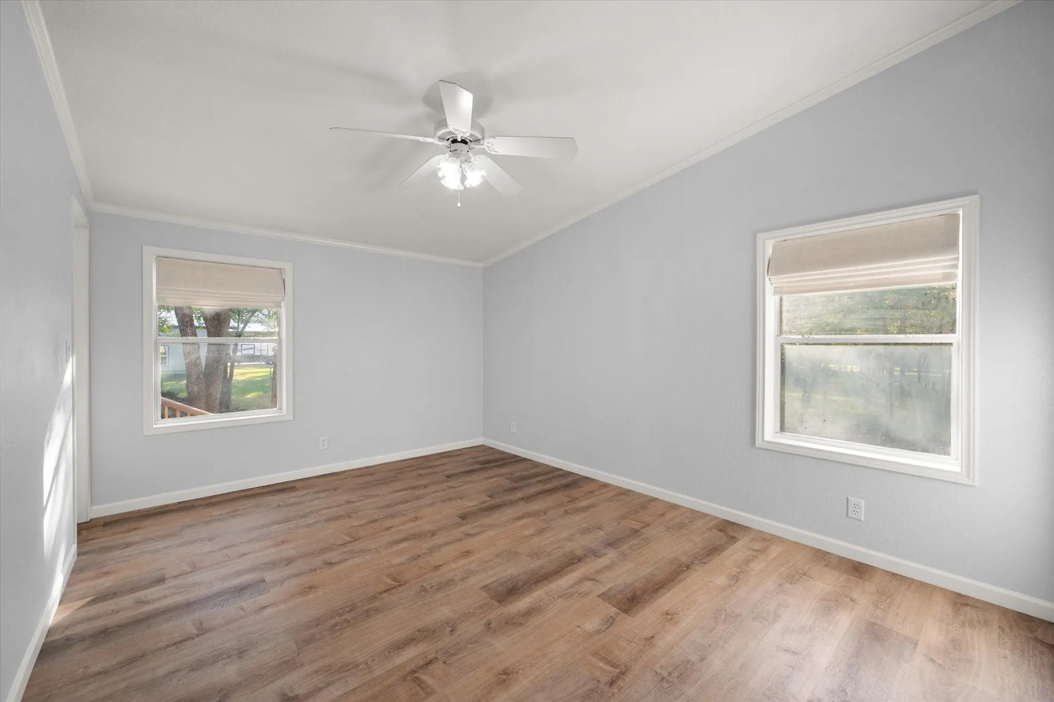 Vaulted ceiling with a ceiling fan, wood-finish flooring, and two windows with blinds