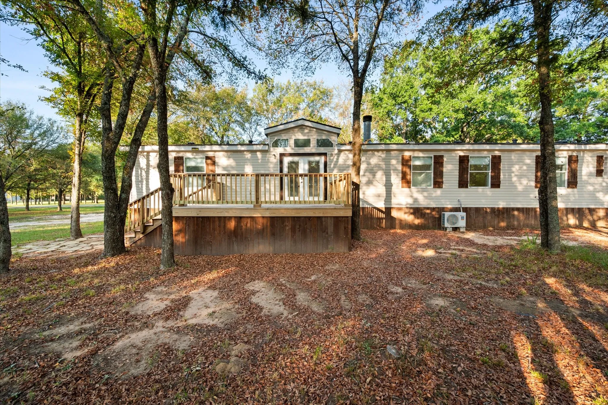 White siding exterior with brown shutters, featuring a prominent wood deck with railings and steps