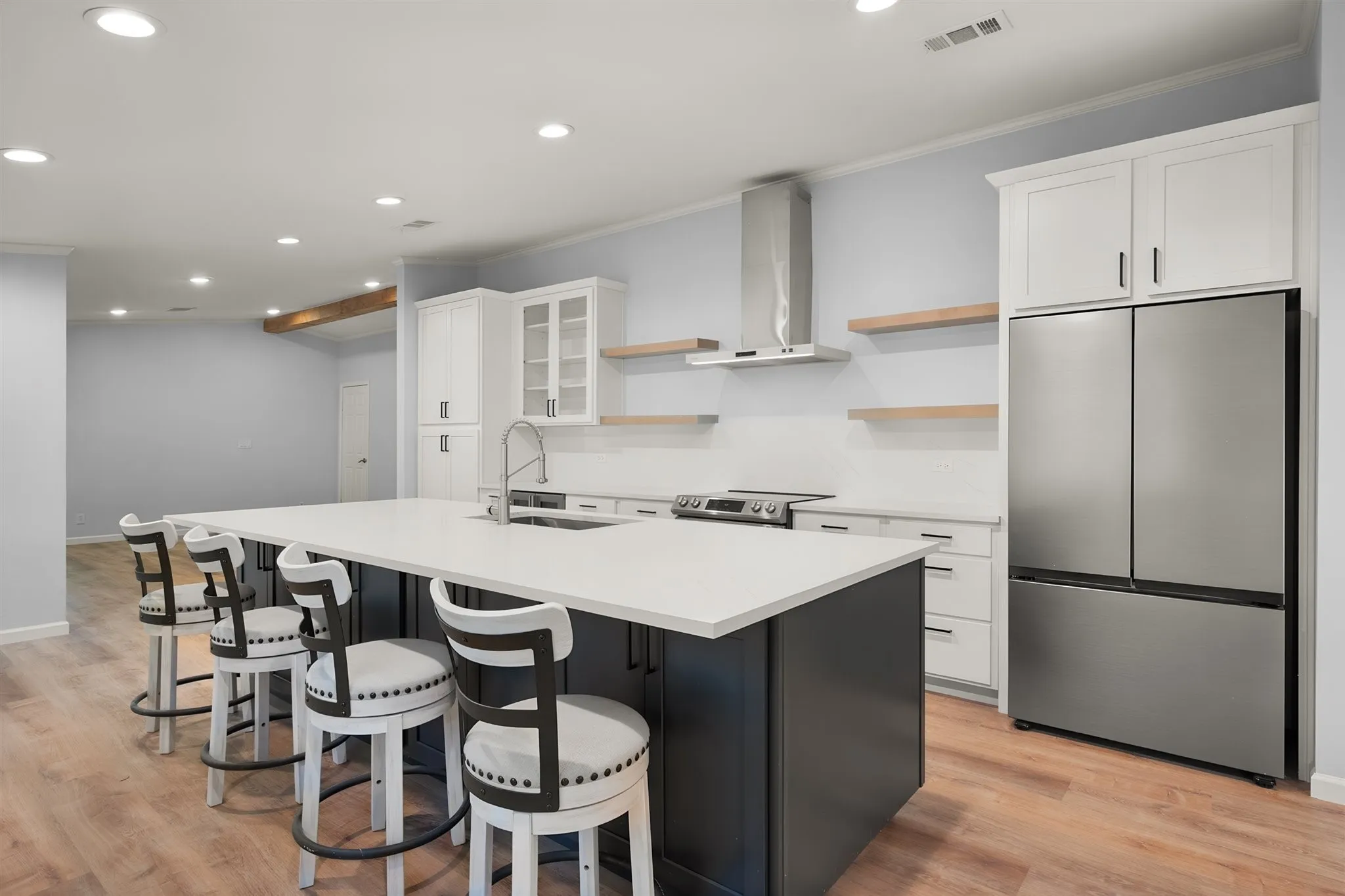 Kitchen featuring a large central island with seating, stainless steel appliances, white cabinetry, and wood-finish flooring