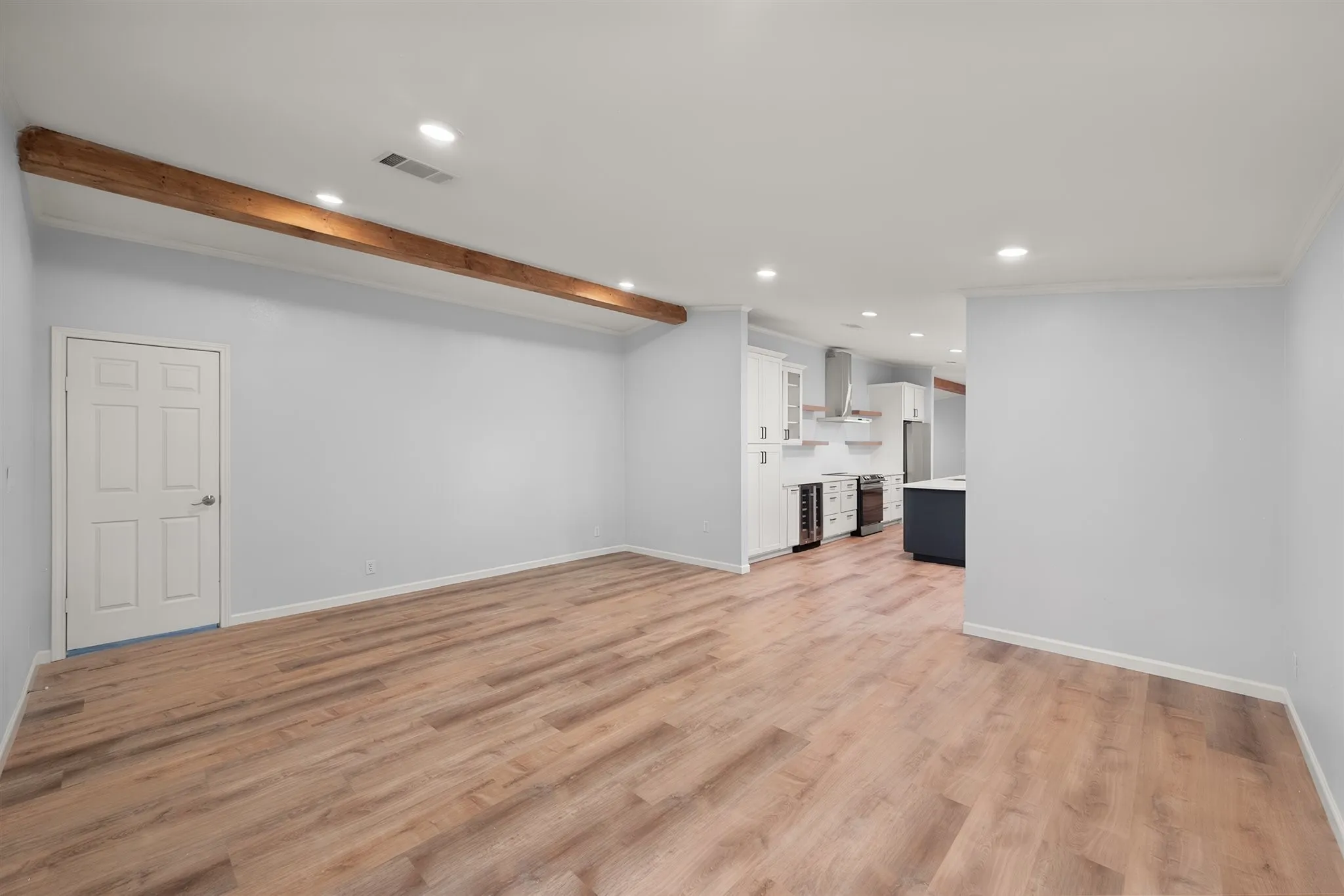 Open-concept living area featuring wood-finish flooring, recessed lighting, and a decorative exposed beam