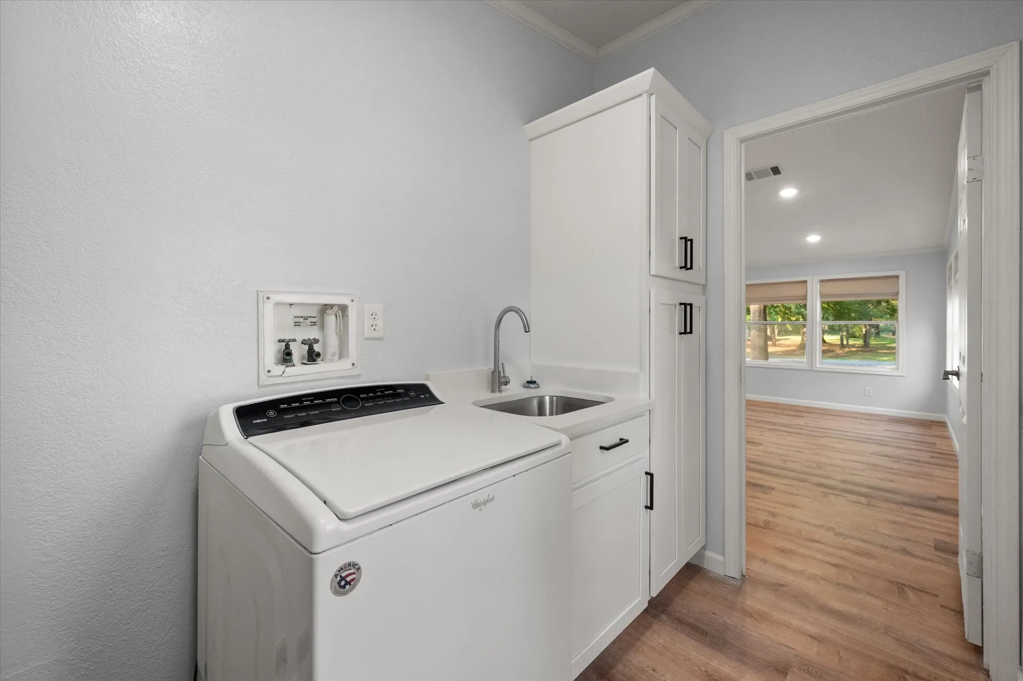 Dedicated laundry area with built-in cabinetry, utility sink, and wood-finish flooring