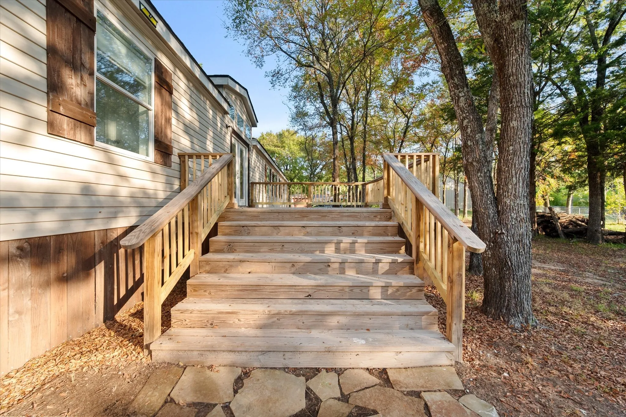 Wooden deck stairs leading to a spacious outdoor deck, featuring natural wood railings and a flagstone pathway