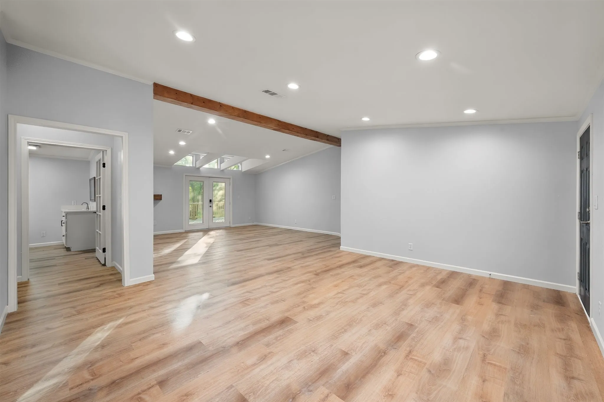 Spacious room featuring wood-finish flooring, exposed wood beam, recessed lighting, and a vaulted ceiling with skylights