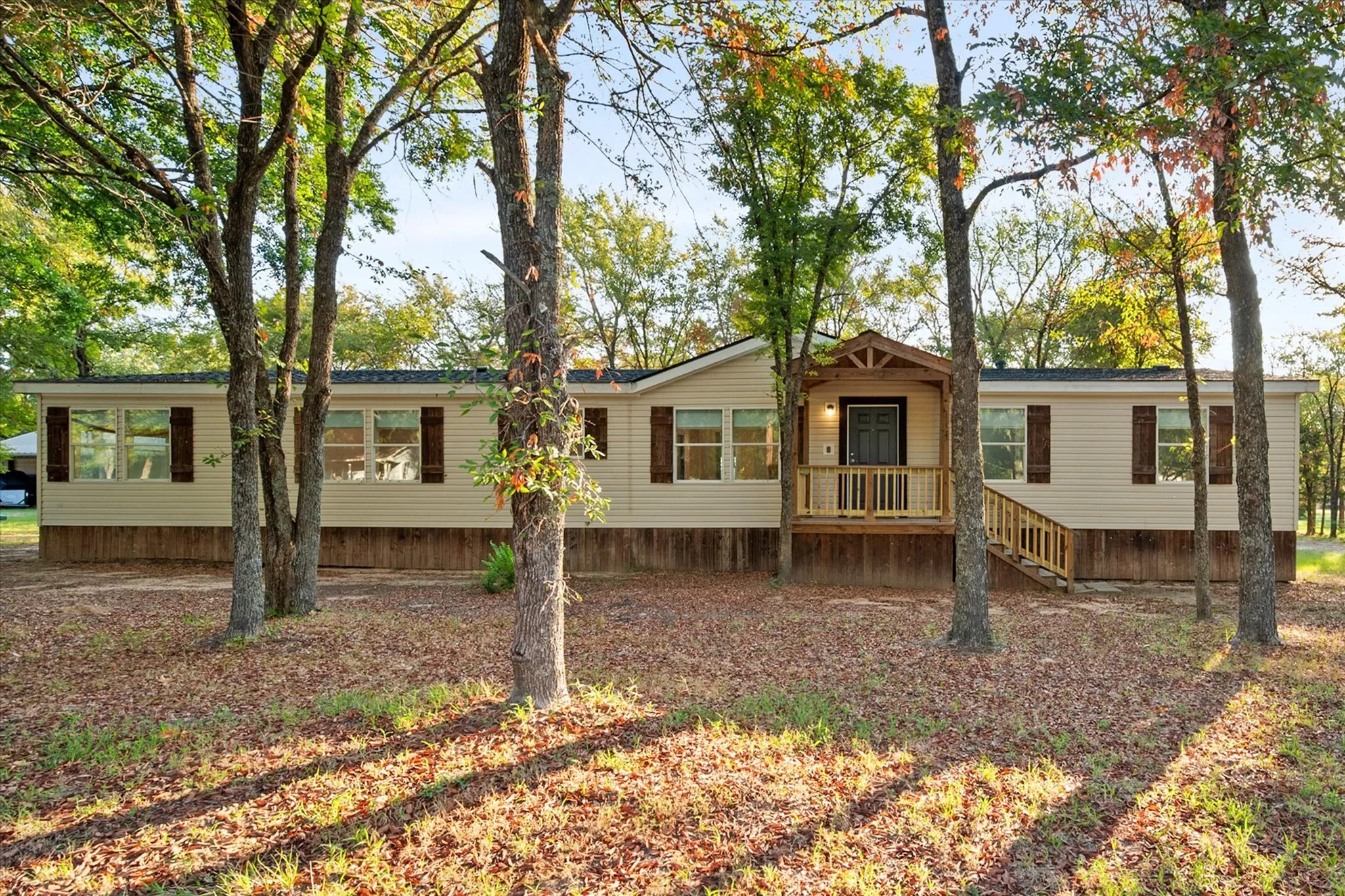 Single-story residence featuring light-toned horizontal siding, dark window shutters, and a covered porch entry with a wood railing and steps