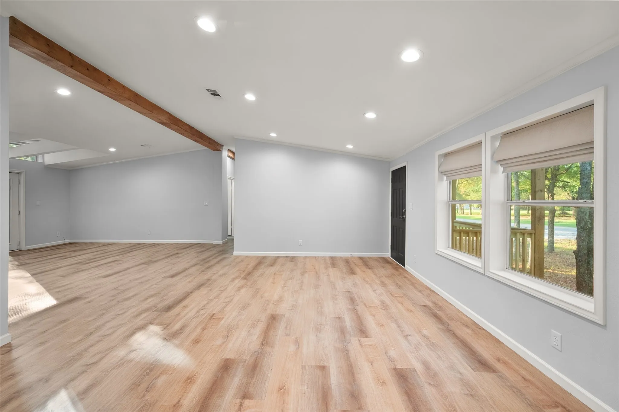 Wood-finish flooring throughout, recessed ceiling lighting, a prominent exposed wood beam, and multiple windows with roller shades