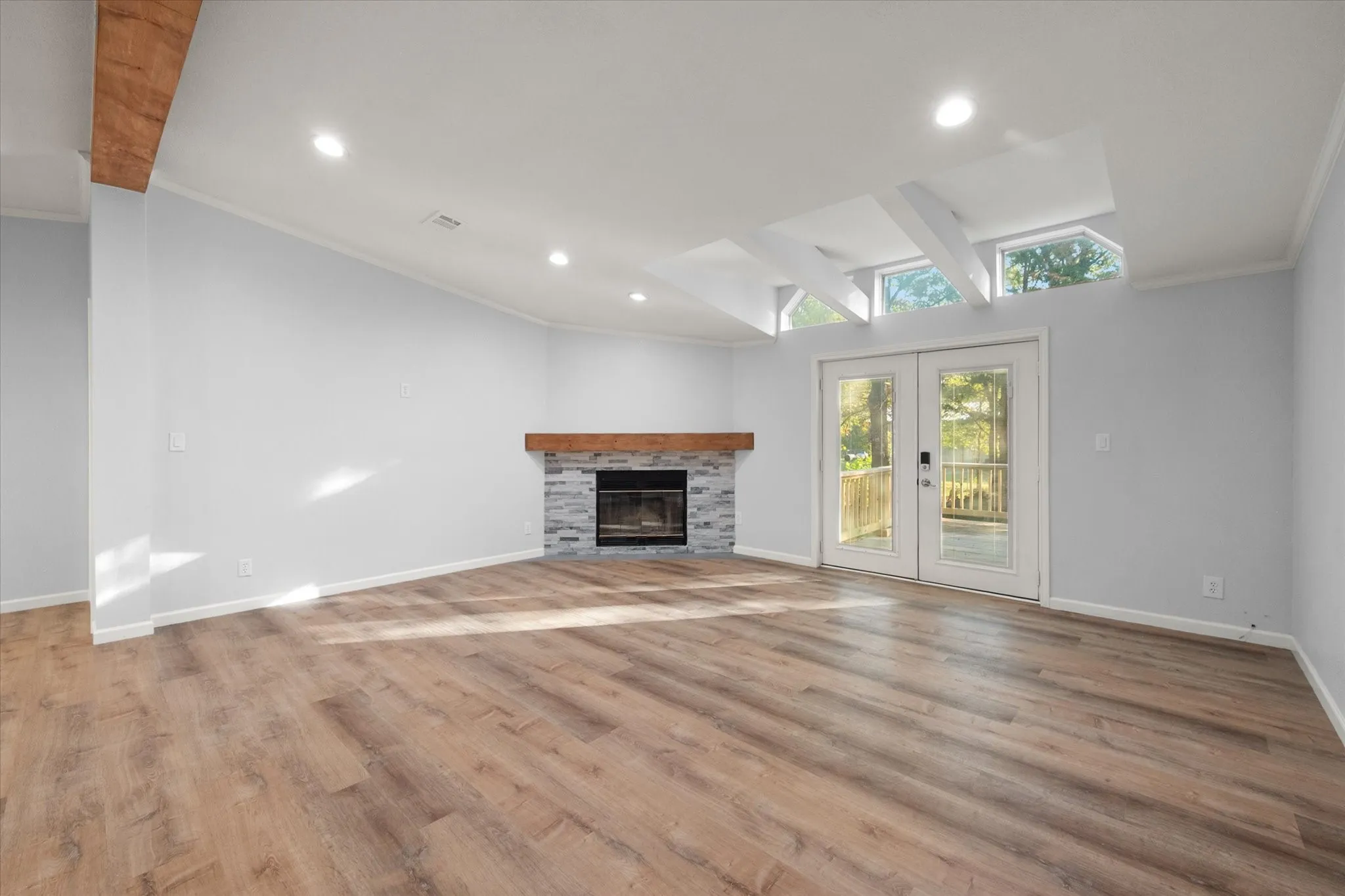 Wood-finish flooring, vaulted ceiling with exposed beams, recessed lighting, and a fireplace with a wood mantle and stone surround