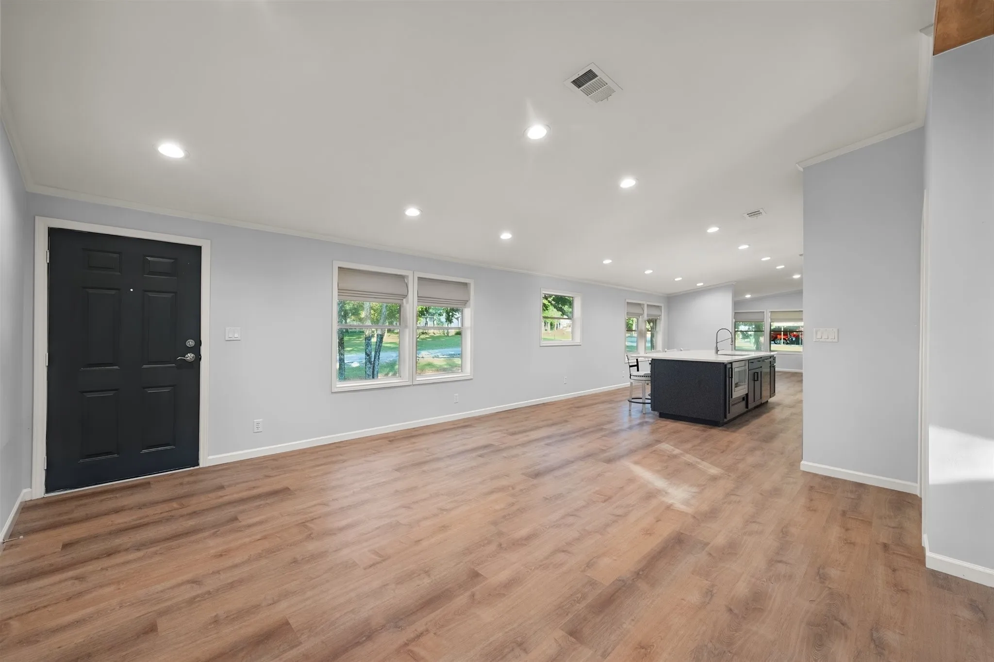 Open-concept living area featuring wood-finish flooring, recessed lighting, and a kitchen island with a sink