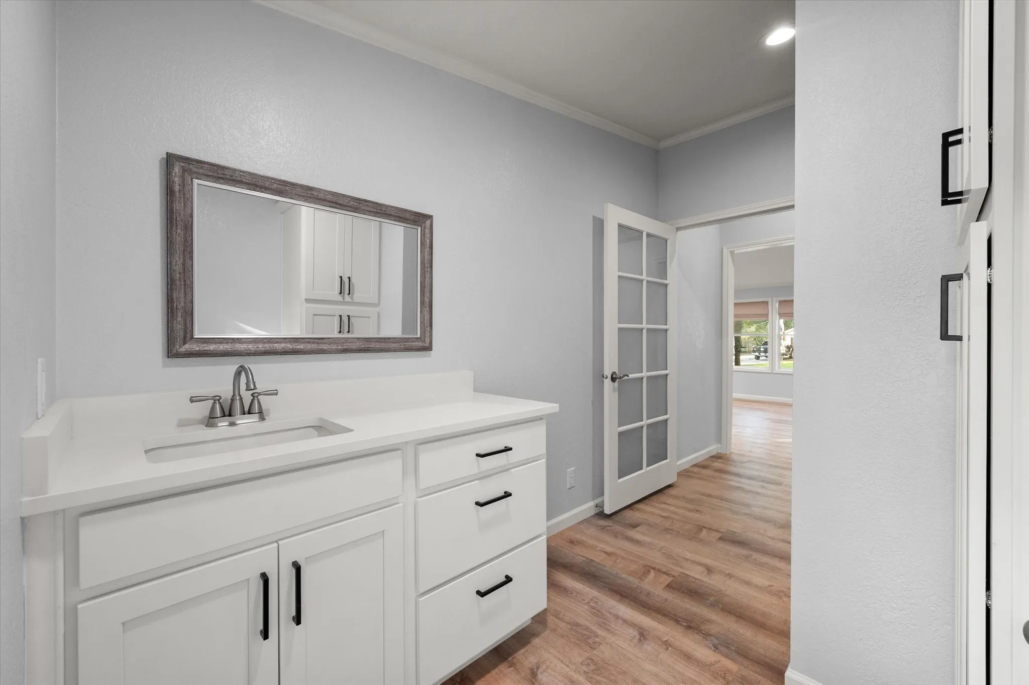 White vanity with integrated sink, white countertop, brushed nickel faucet, and rustic-framed mirror