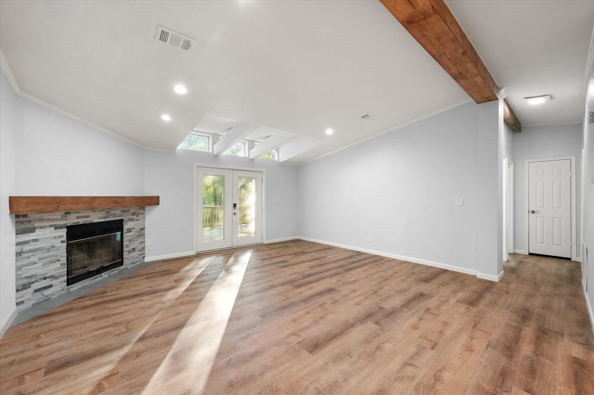Vaulted ceiling with exposed beam, recessed lighting, stone-clad fireplace with wood mantle, wood-finish flooring, and double French doors to the exterior