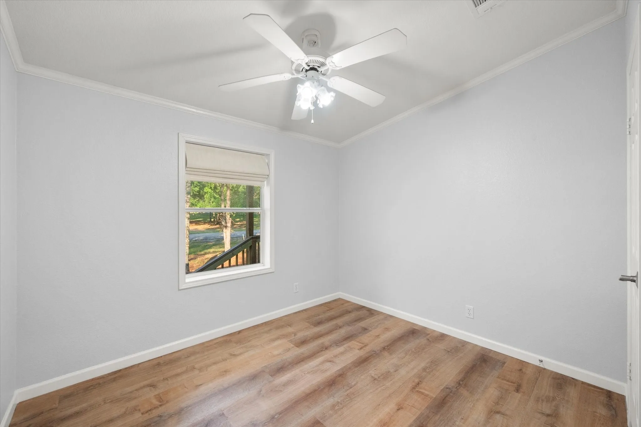 Wood-finish flooring, white trim, ceiling fan, and a window with natural light