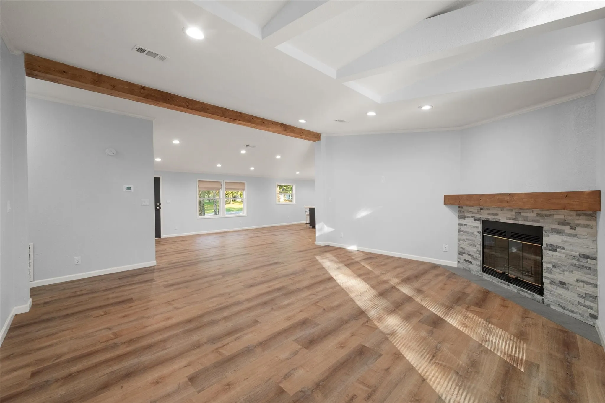 Recessed lighting, wood-finish flooring, exposed wood beams, a fireplace with stone surround, and tray ceilings