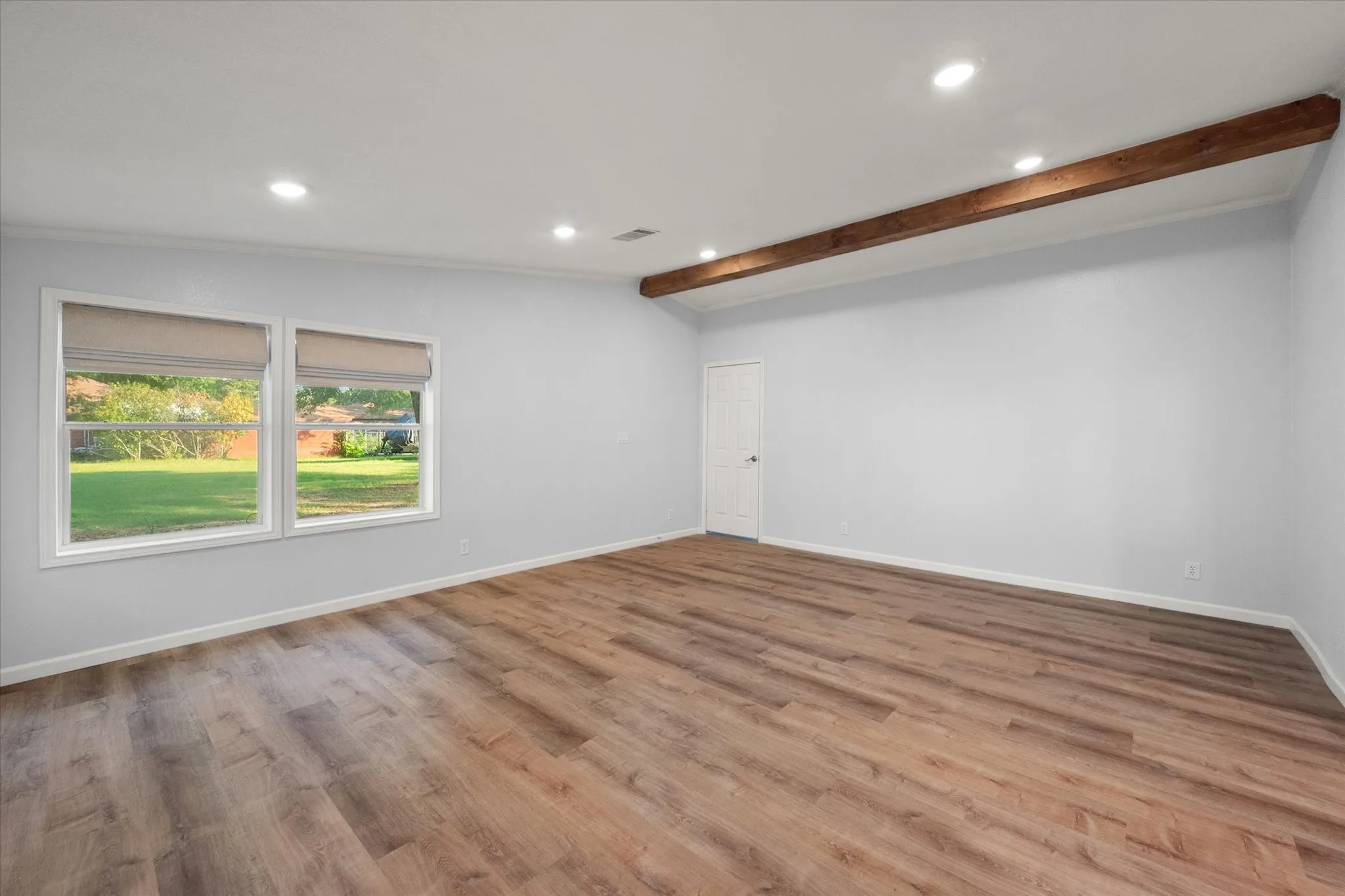 Wood-finish flooring, two large windows, recessed ceiling lighting, and a visible wood beam