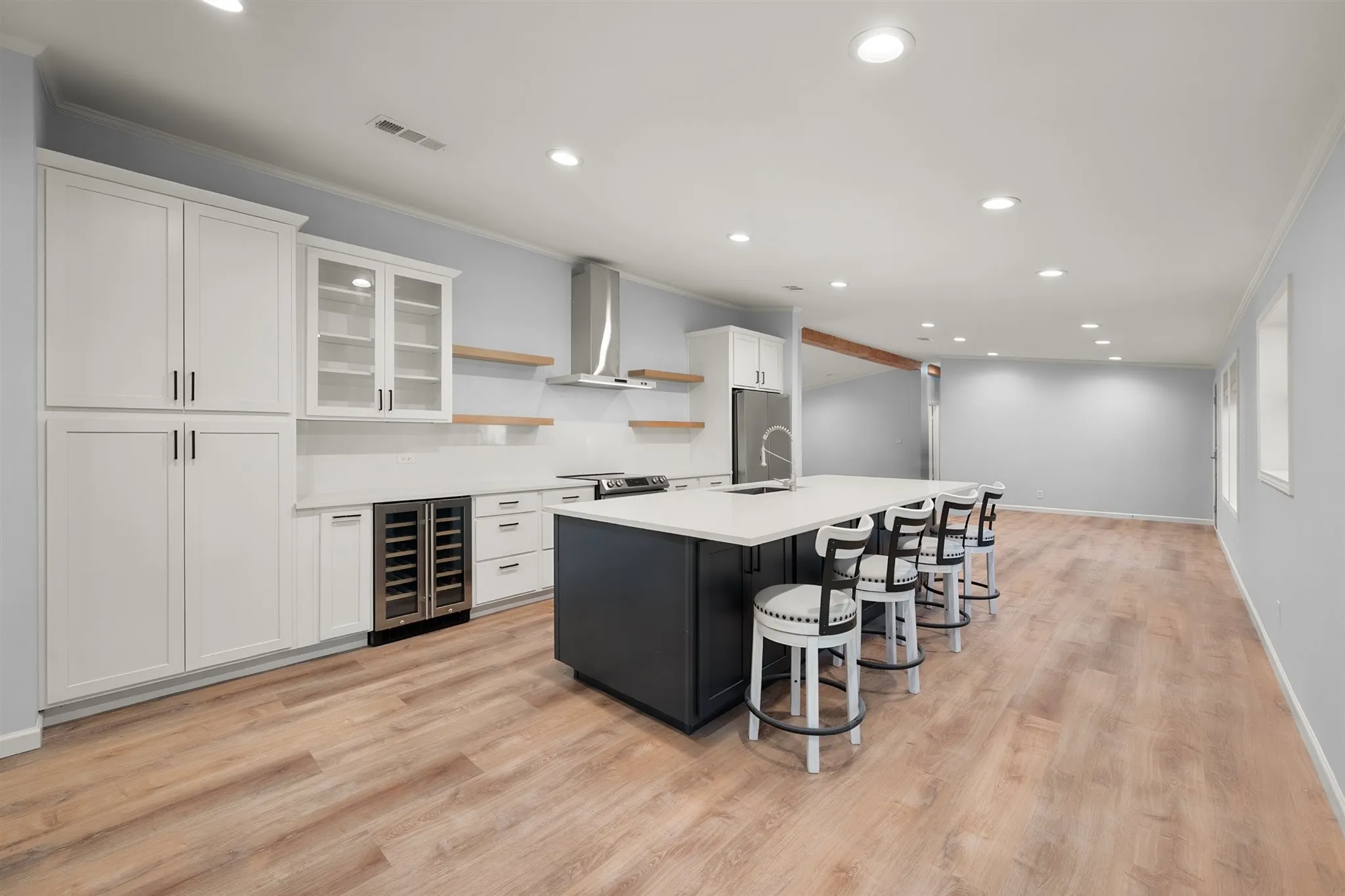 Spacious kitchen featuring an extended island with a built-in sink, white cabinetry with glass-front uppers, a beverage cooler, and wood-finish flooring