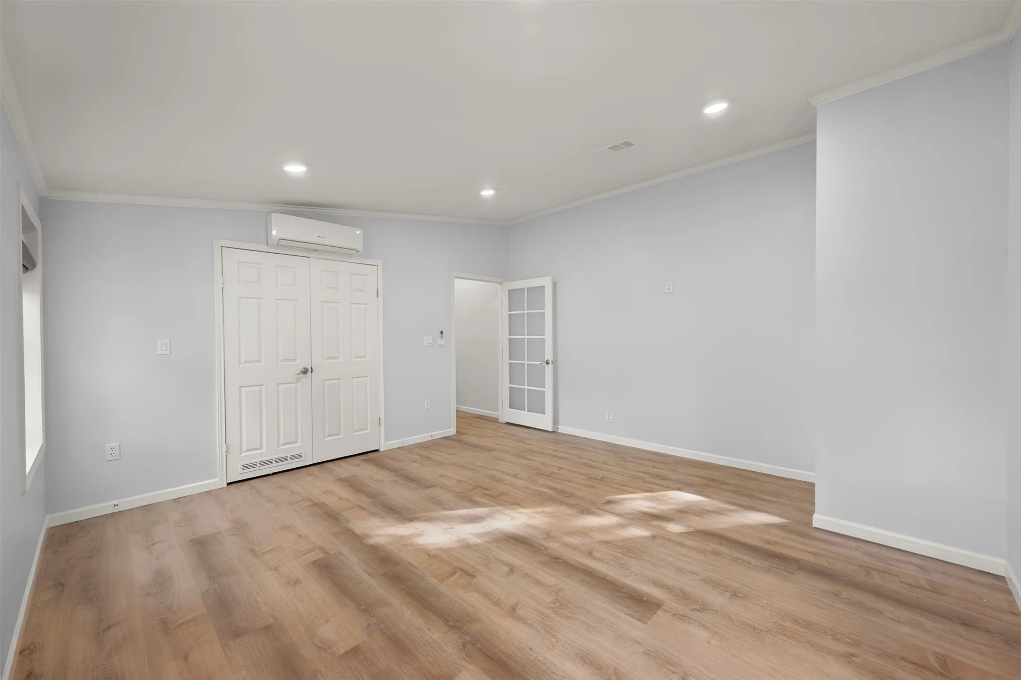 Spacious room featuring wood-finish flooring, recessed lighting, a mini-split system, double panel doors, and a French door entry