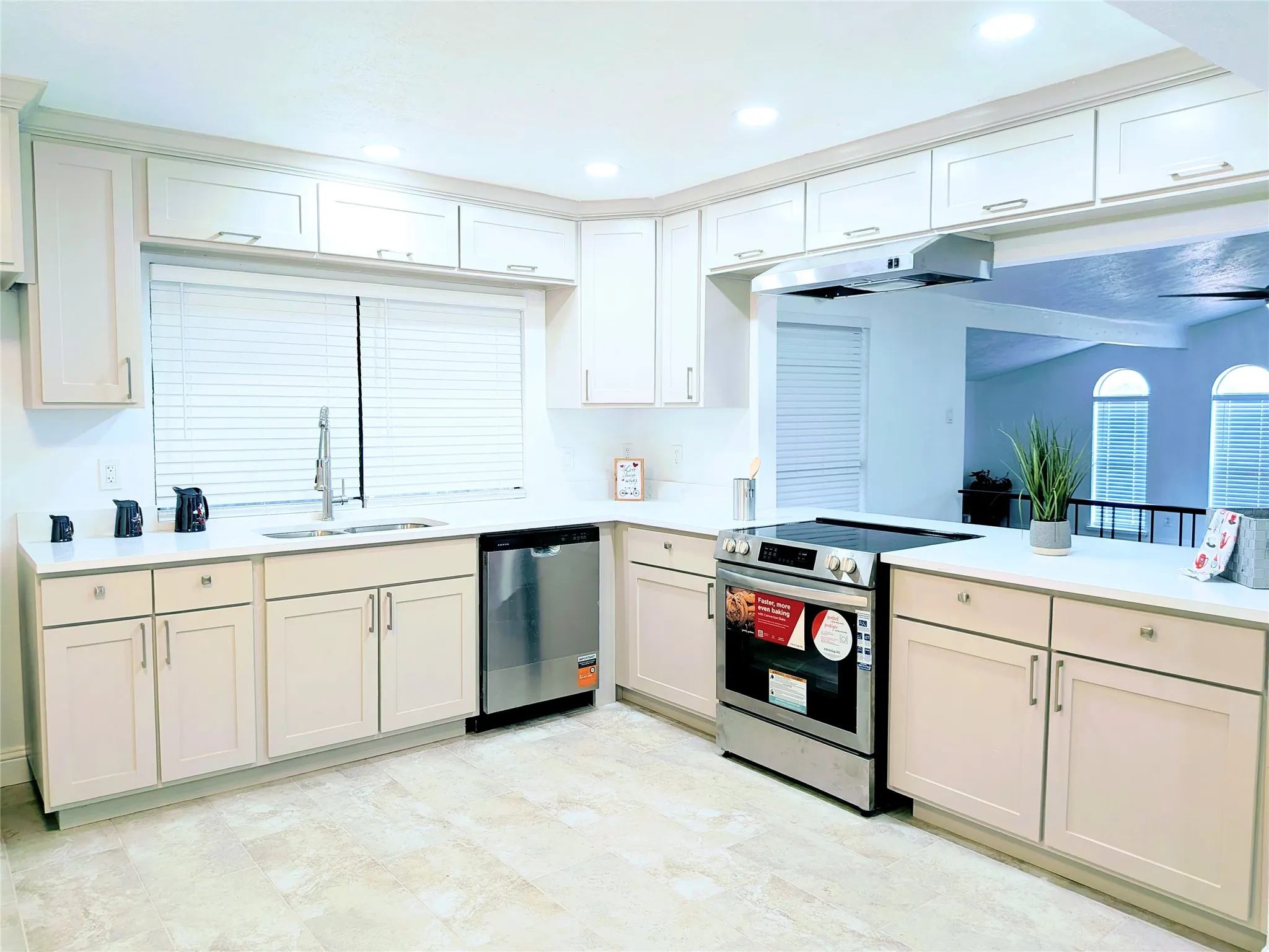 Contemporary kitchen featuring extensive cabinetry, stone countertops, a stainless steel sink with a gooseneck faucet, a built-in dishwasher, and a range with an overhead exhaust hood