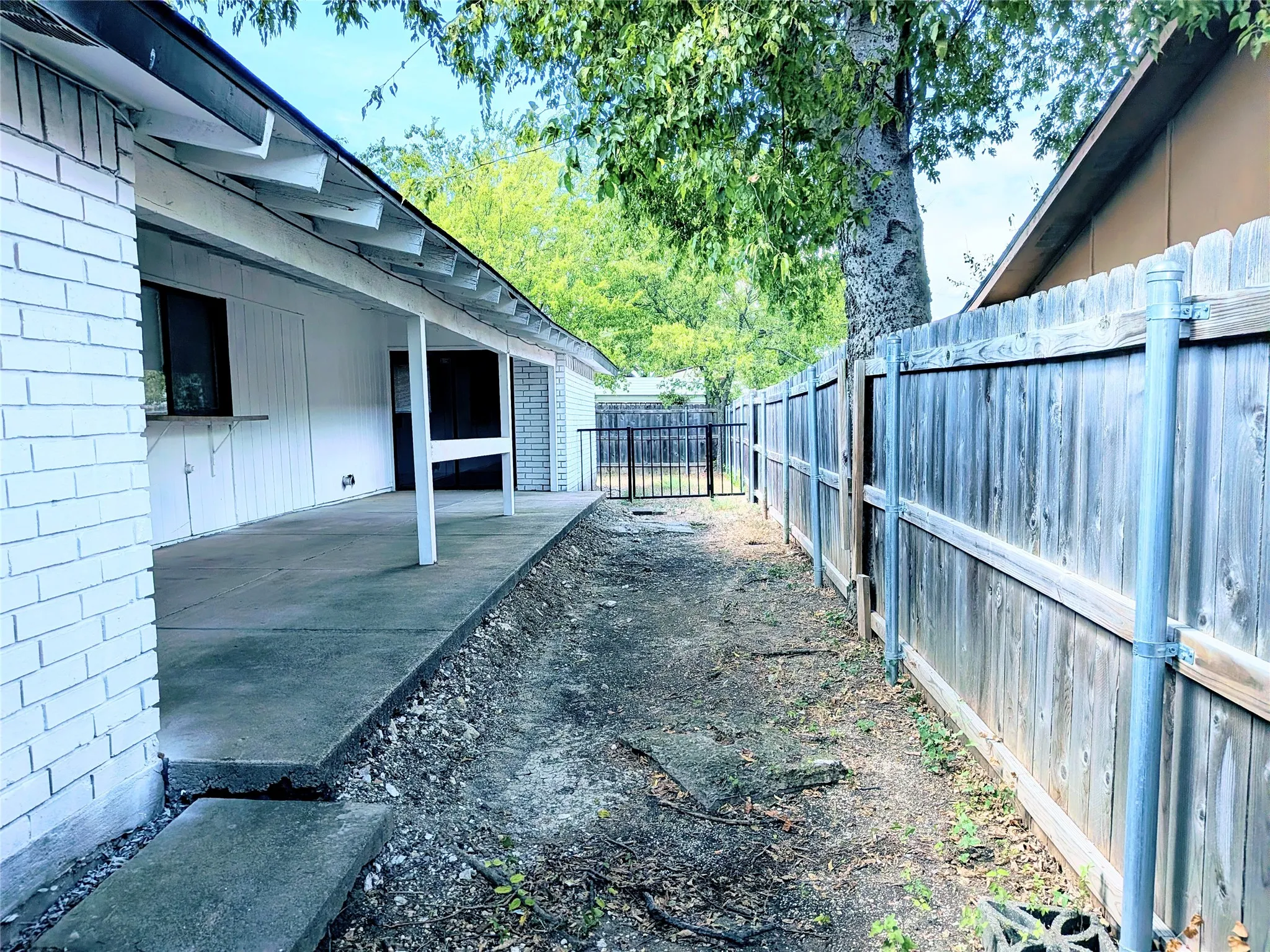 Covered patio with concrete flooring, white brick exterior, and a wood privacy fence