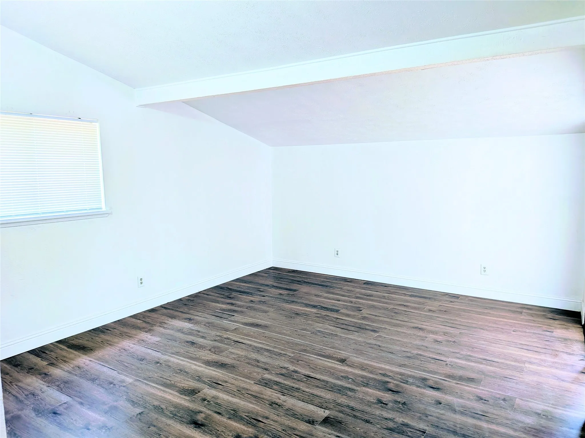 Wood-finish flooring with white walls and a window with horizontal blinds