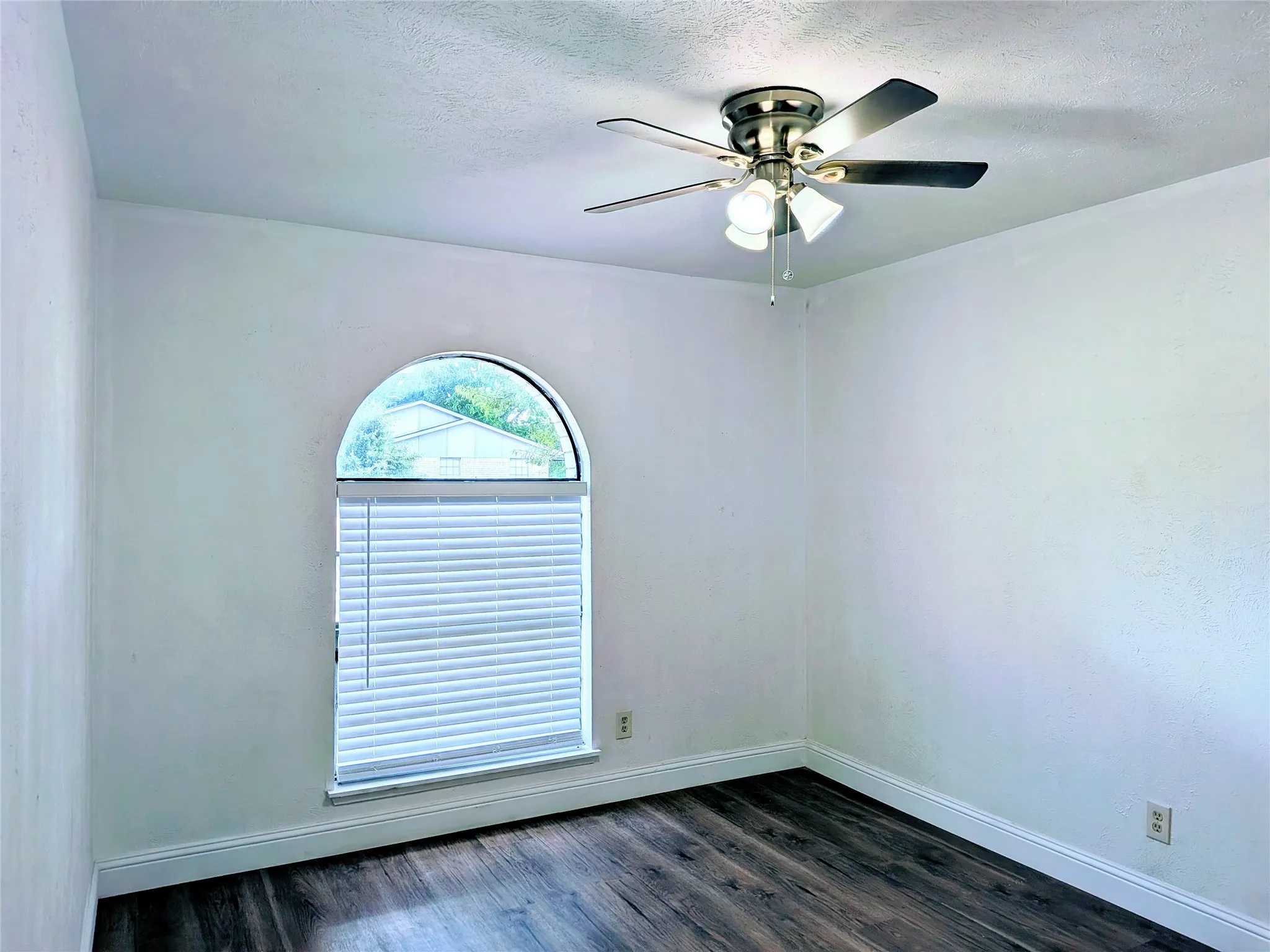 Arch-top window with blinds, wood-finish flooring, ceiling fan with integrated lighting, and white wall finishes