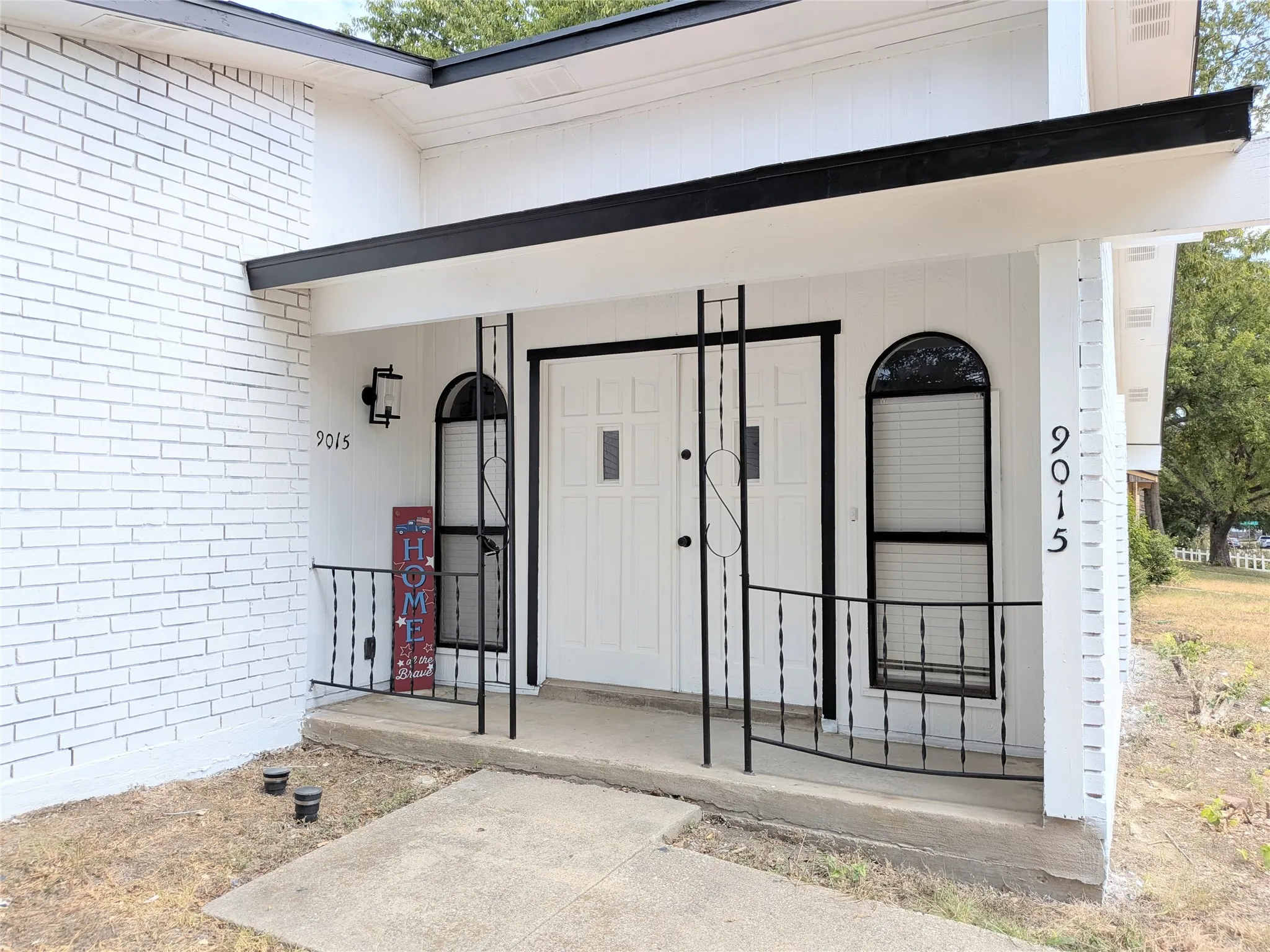 White brick exterior with a covered entry, wrought iron railing, and arched window details