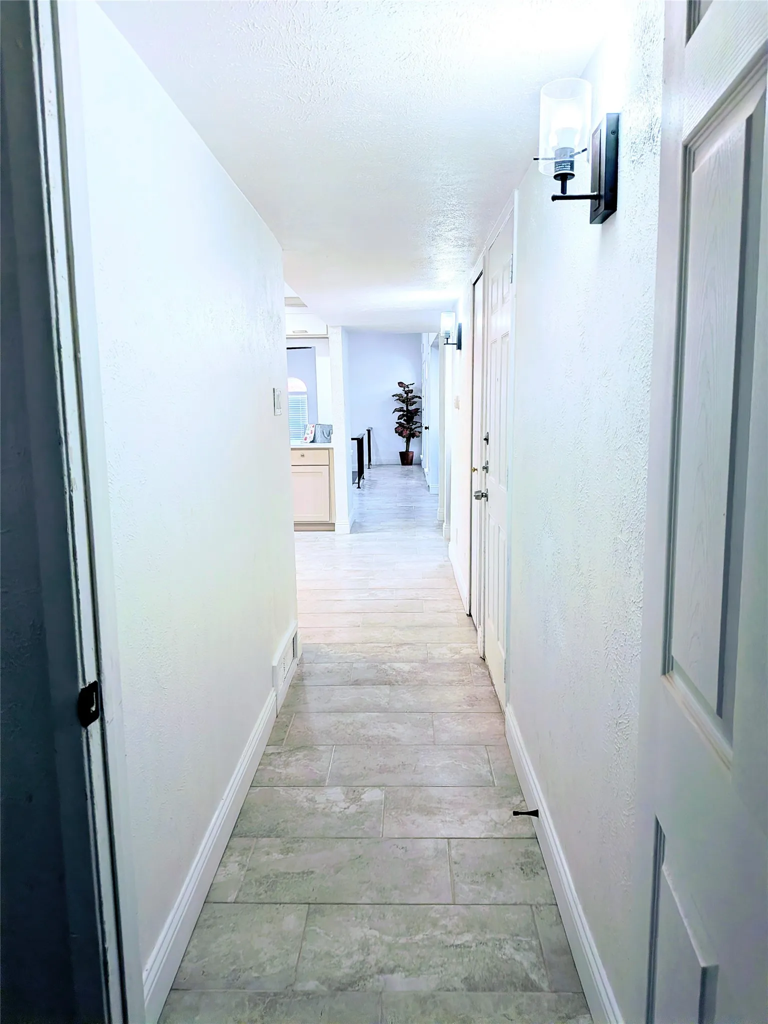 Hallway featuring light-toned tile flooring, recessed ceiling lighting, and wall-mounted sconces