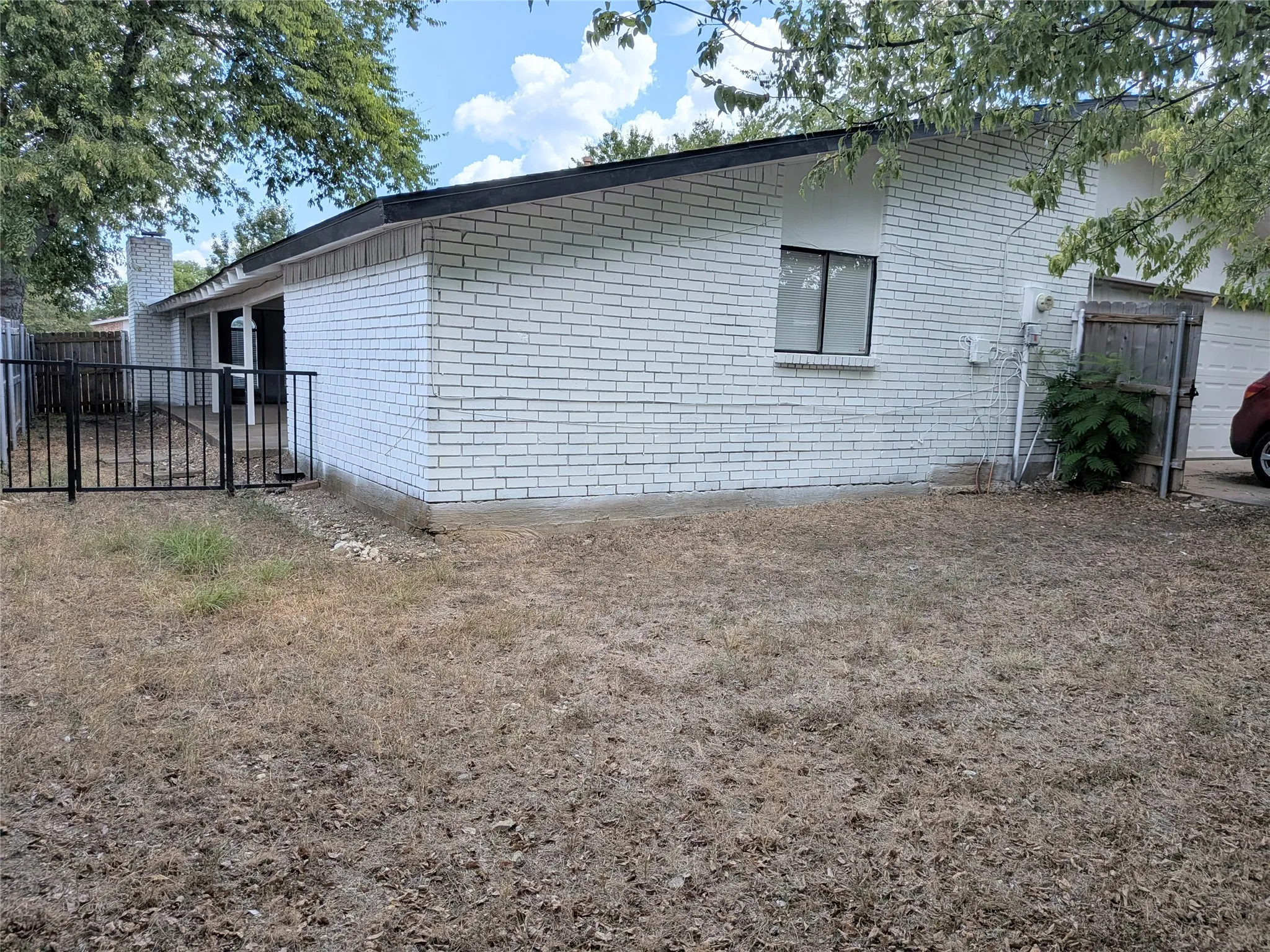 White brick exterior with a black roofline, fenced patio area, and an exposed brick chimney