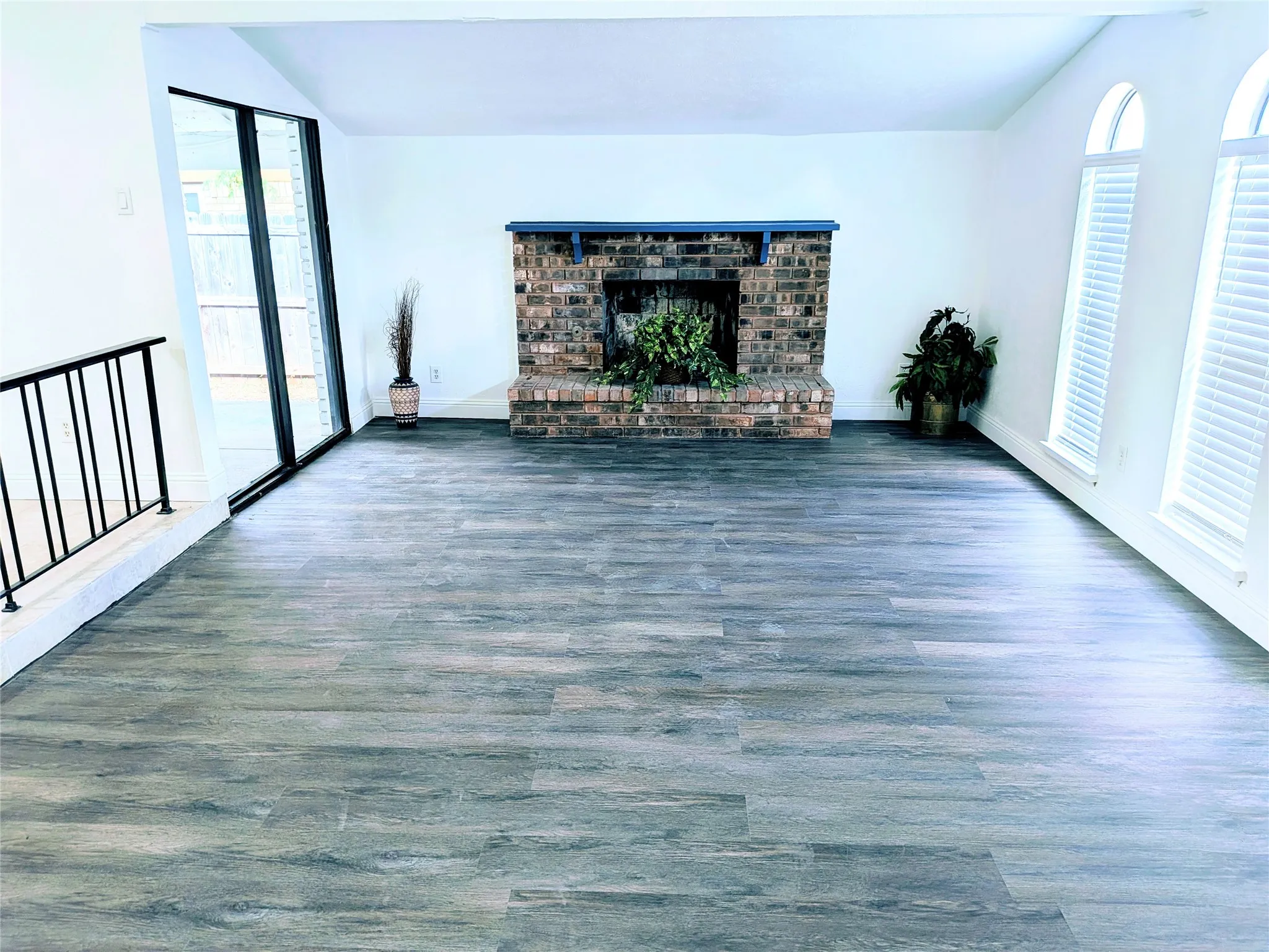 Spacious interior featuring wood-finish flooring, a brick fireplace with a mantle, and multiple arched windows