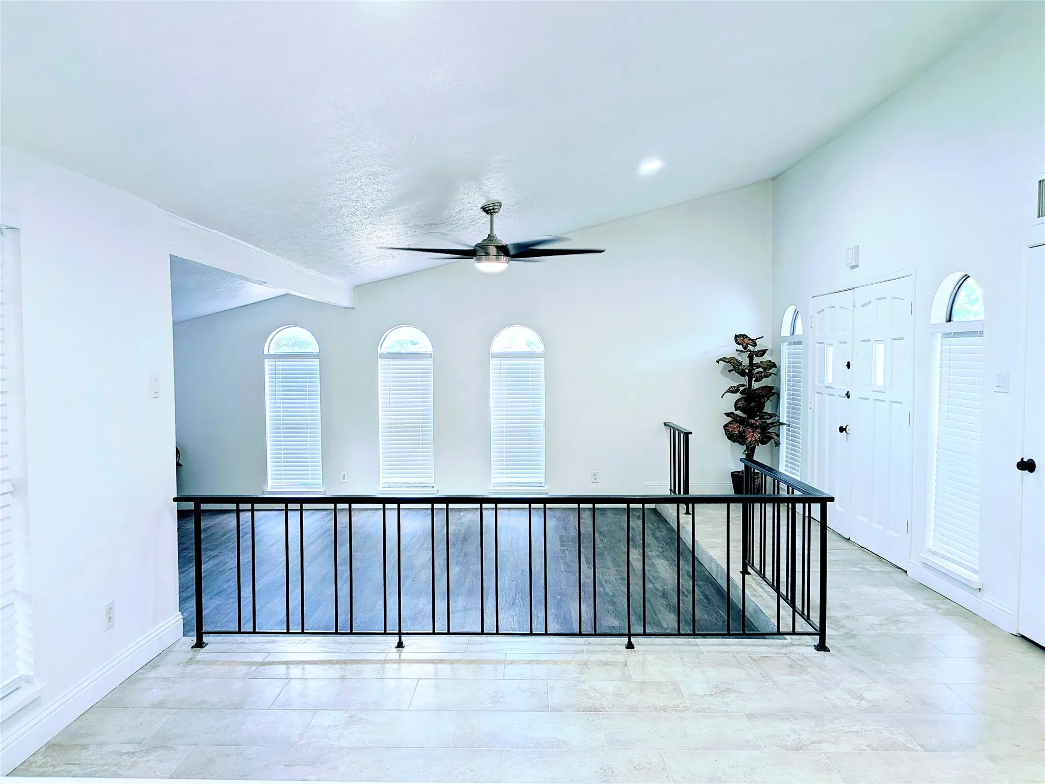 Vaulted ceiling with a ceiling fan, arched windows with blinds, wood-finish flooring, white paneled doors, and wrought iron railing