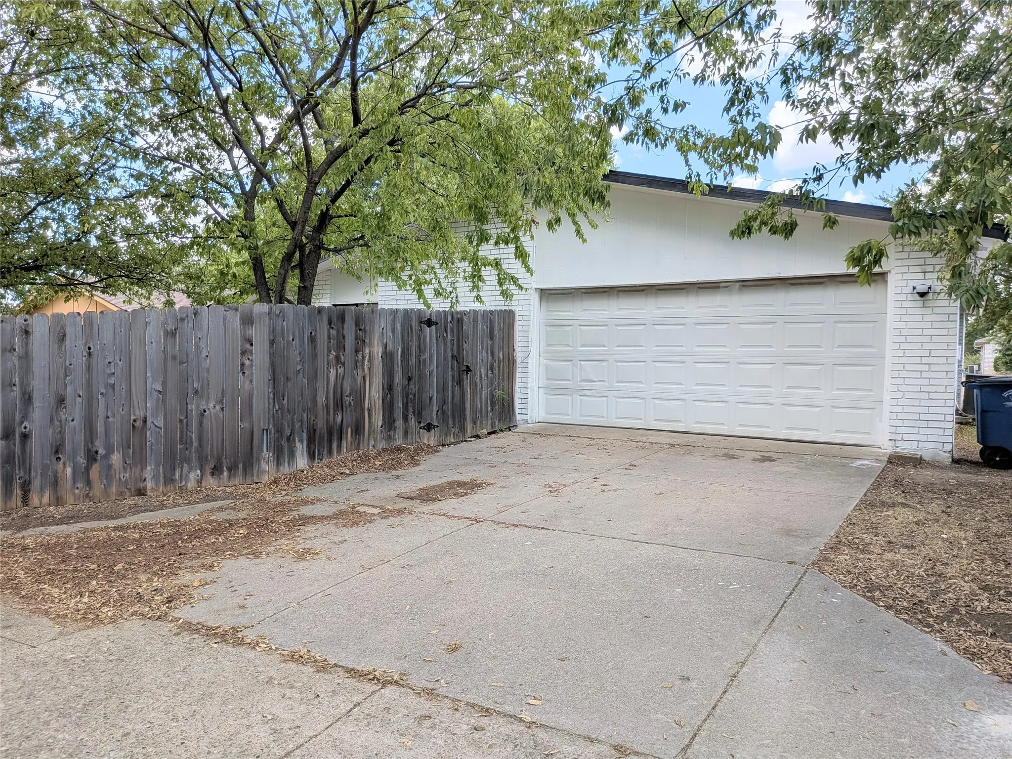 Attached two-car garage with white paneled door, concrete driveway, white brick exterior accents, and wood privacy fence