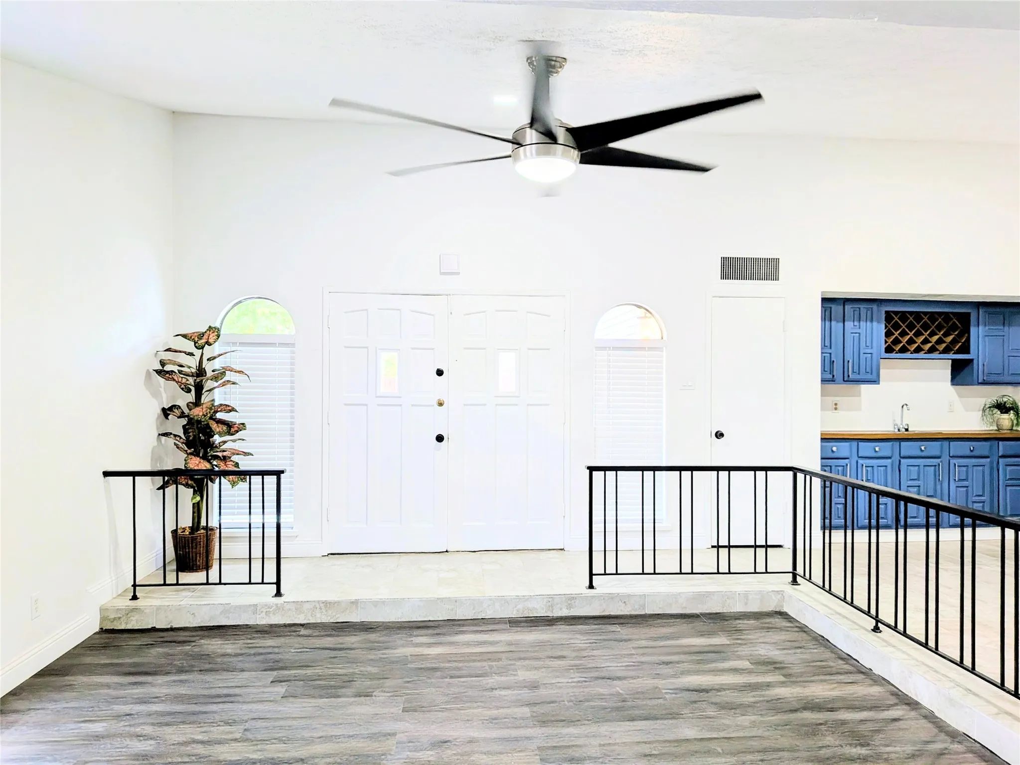 Wood-finish flooring, vaulted ceilings, modern ceiling fan, double entry doors with transom windows, and built-in blue cabinetry with wood-finish countertops