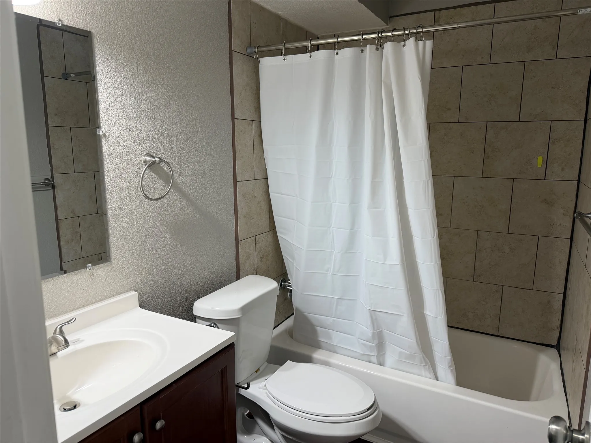 Bathroom featuring a tiled shower surround, integrated bathtub, white vanity with a single basin, and a wall-mounted mirror