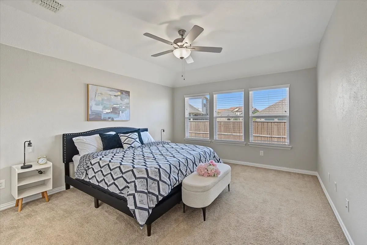 Tray ceiling with a ceiling fan and light fixture, three windows with blinds, and light-colored carpeting