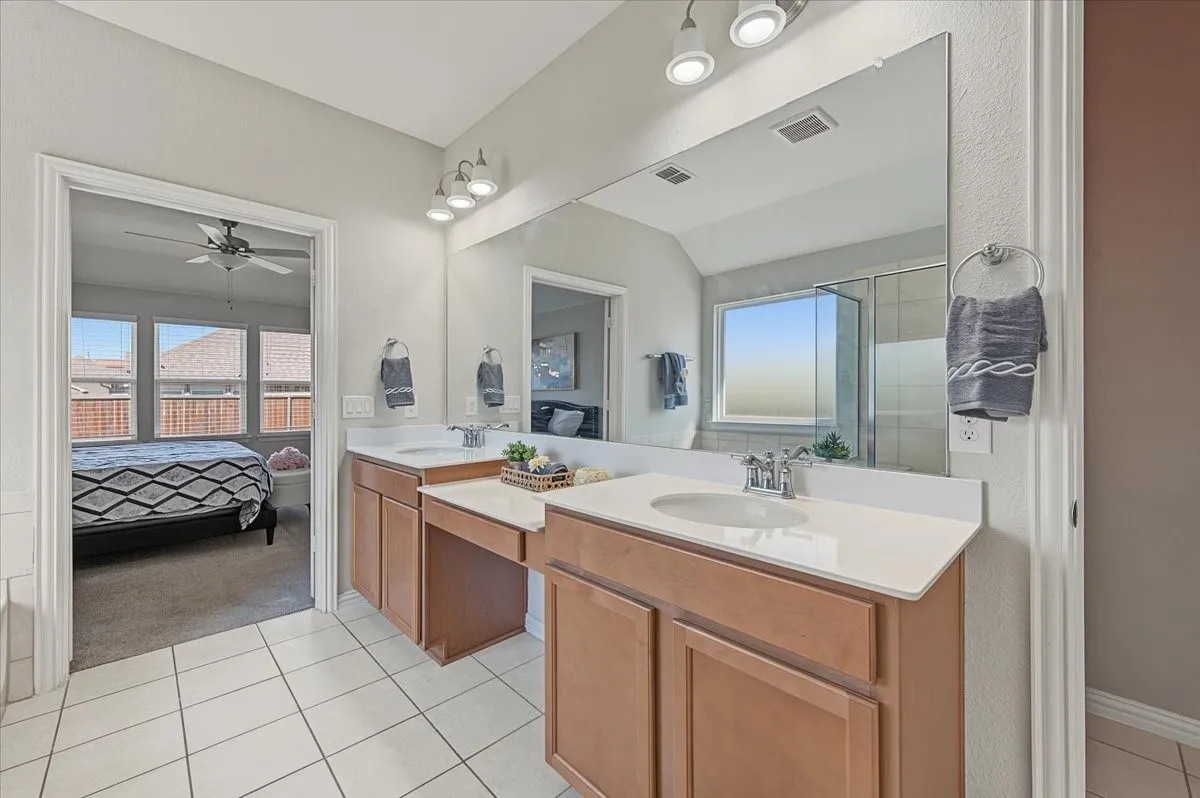Dual vanities with integrated sinks and chrome fixtures, expansive mirror, wood-finish cabinetry, and tiled flooring
