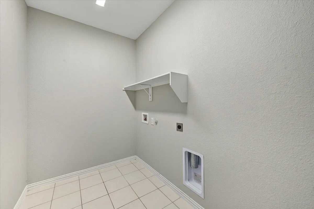 Light-toned walls with a wall-mounted shelf, tile flooring, and integrated laundry hookups