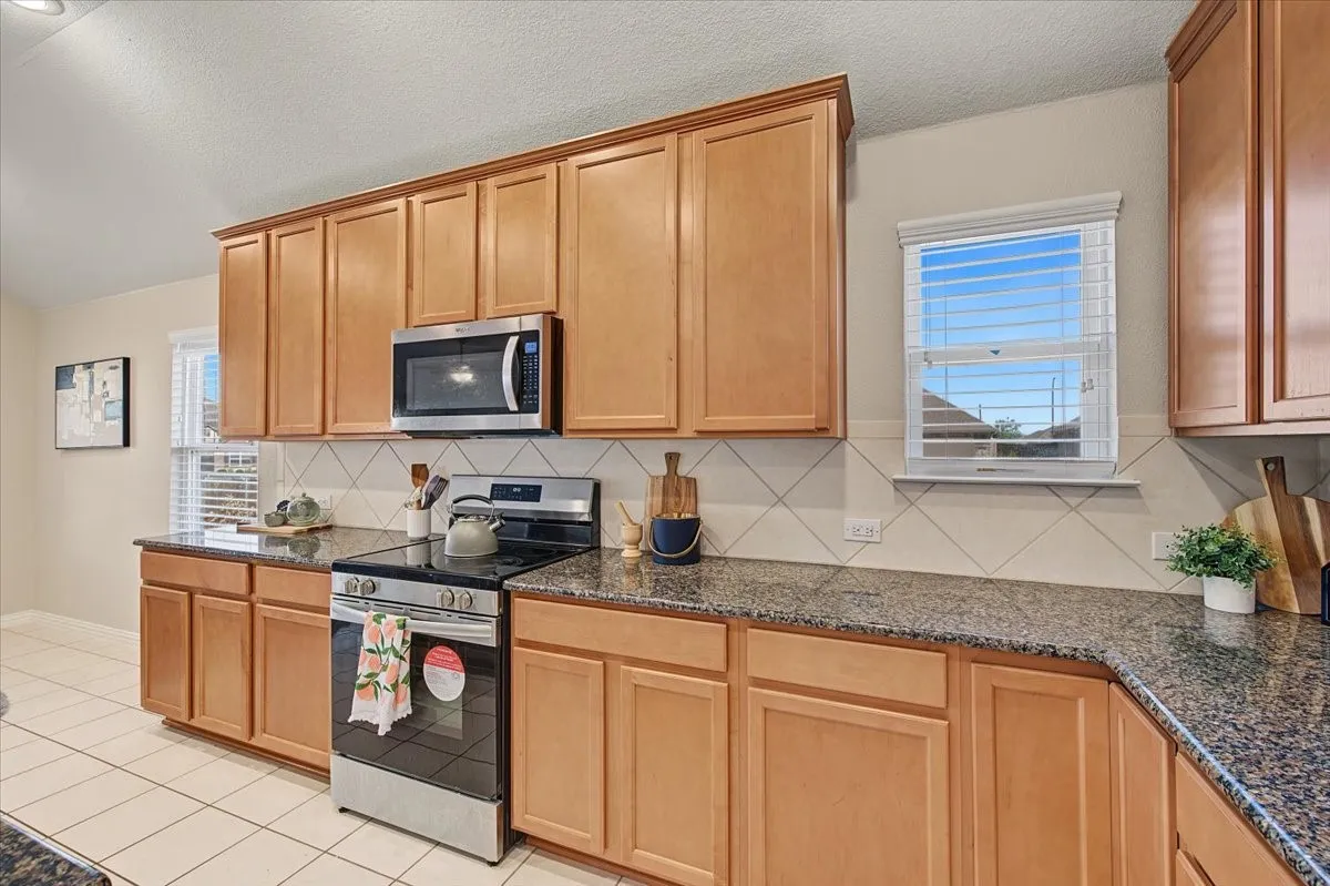 Kitchen featuring wood-finish cabinetry, speckled countertops, diagonal tile backsplash, stainless steel appliances, and tile flooring