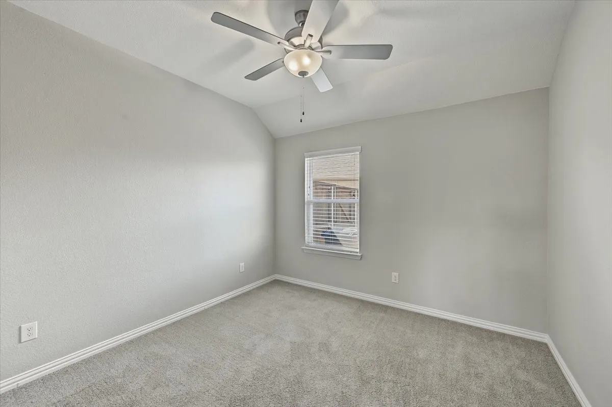 Vaulted ceiling with a ceiling fan light fixture, light gray walls, window with blinds, and gray carpet flooring