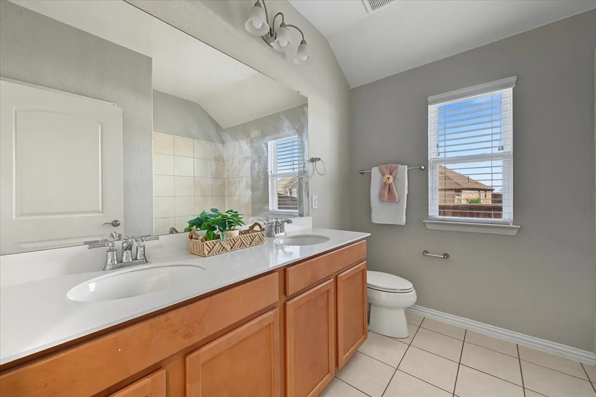 Dual vanity with integrated sinks and chrome fixtures, light wood-finish cabinetry, white countertop, and tiled flooring