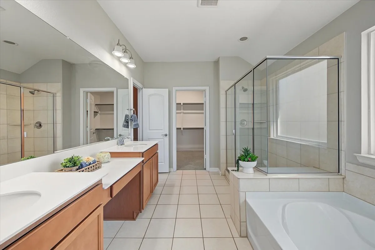 Dual vanities with undermount sinks, separate shower enclosure with glass surround, built-in soaking tub, and tile flooring