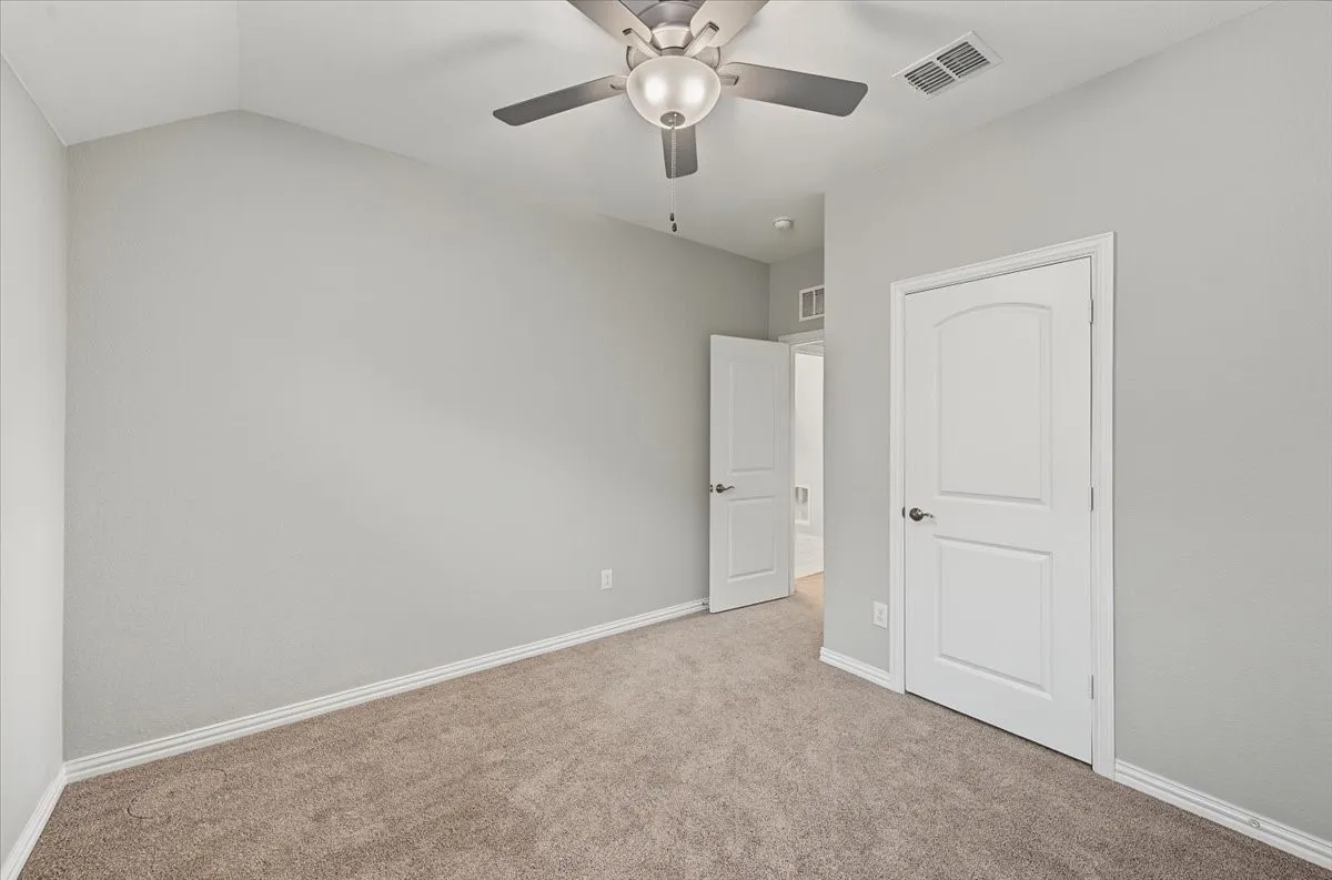 Vaulted ceiling with a flush-mount ceiling fan, neutral wall paint, and soft carpeting