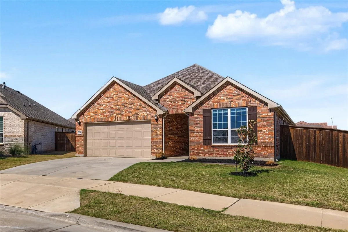 Brick exterior with a gabled roof, attached garage, front yard landscaping, and wood privacy fencing