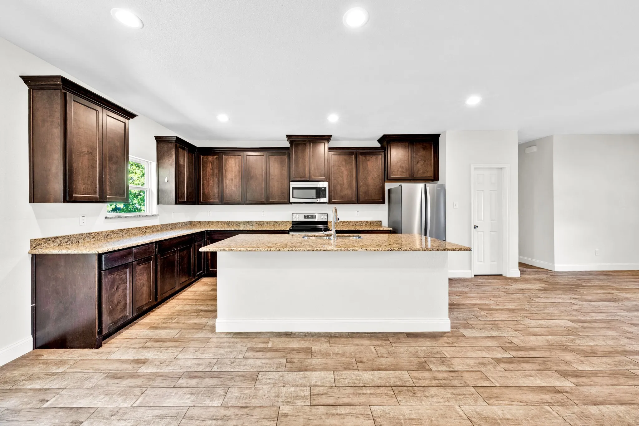 Kitchen featuring dark wood-finish cabinetry, light-toned countertops, a central island, and stainless steel appliances