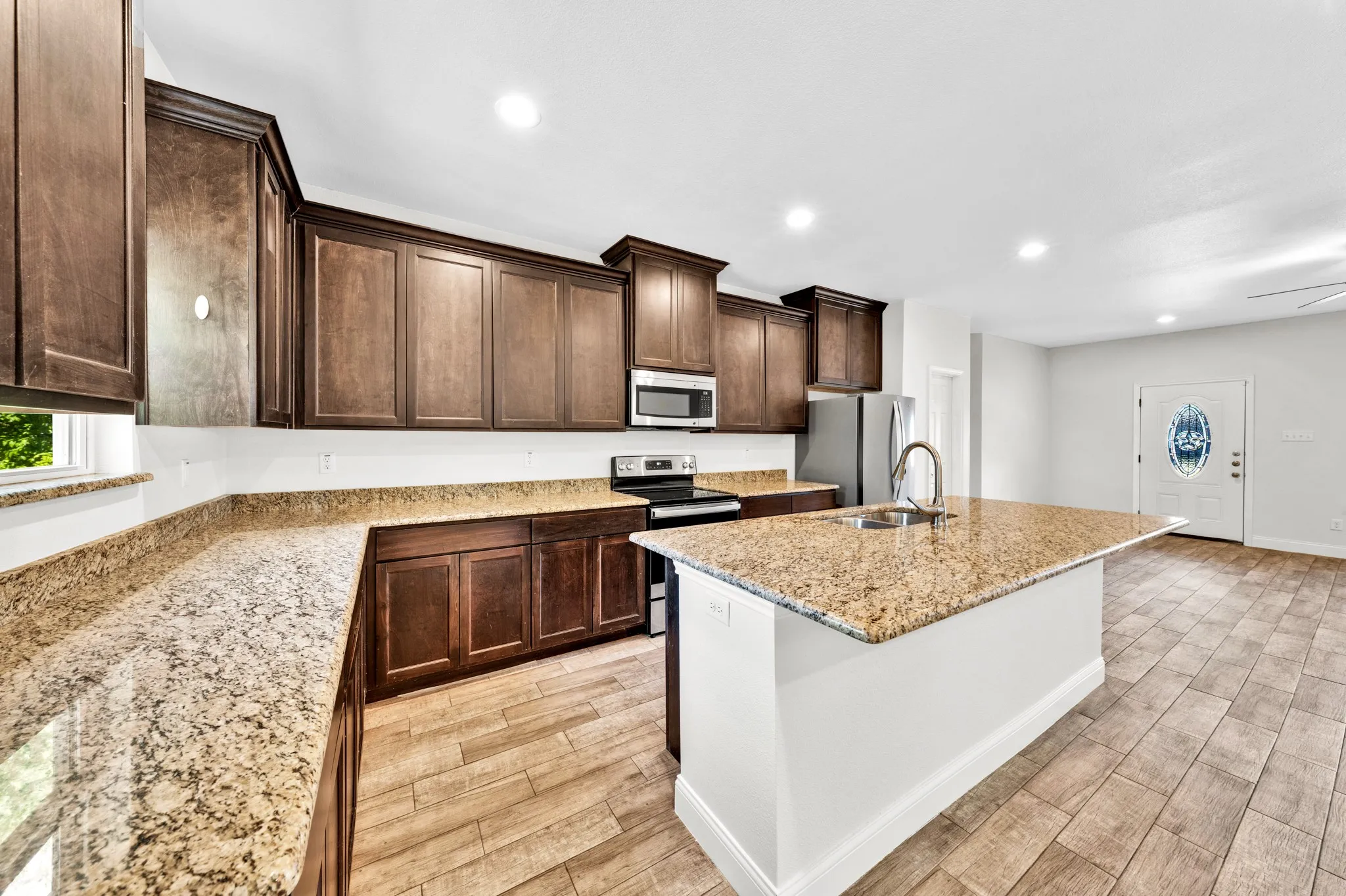 Kitchen featuring wood-finish cabinetry, granite countertops, stainless steel appliances, and a central island with a sink