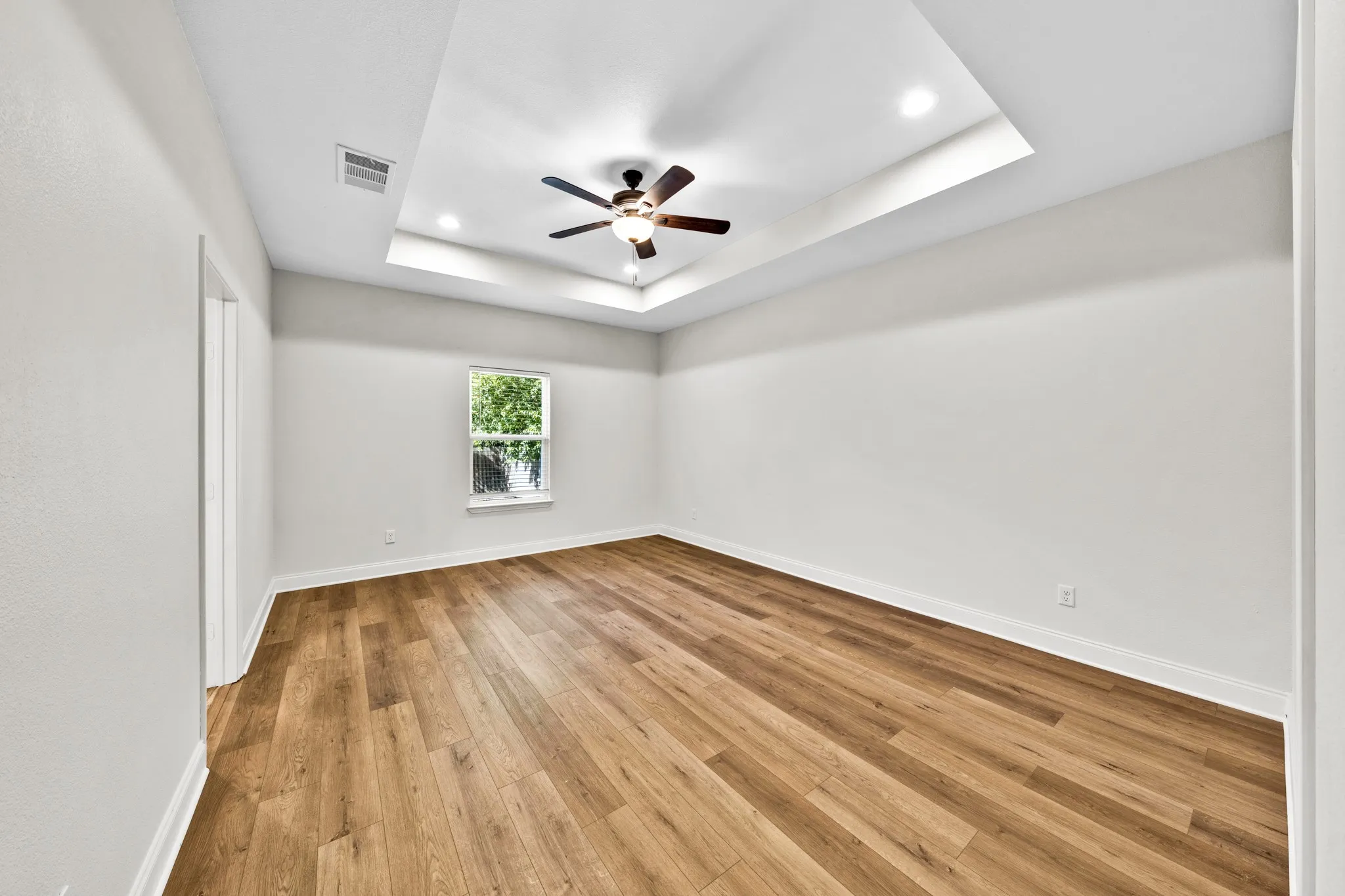 Tray ceiling with recessed lighting and a ceiling fan, wood-finish flooring, white walls, and a window