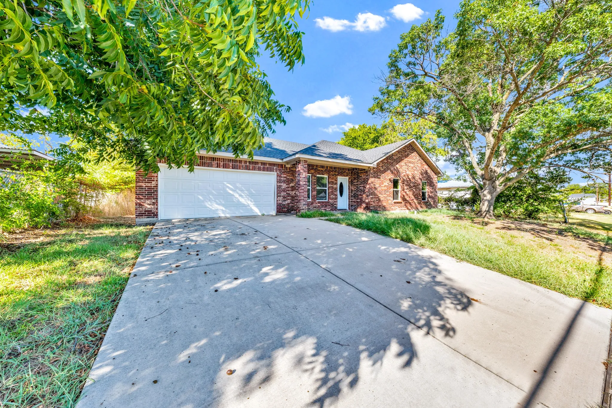 Brick exterior with a white garage door, concrete driveway, and mature trees
