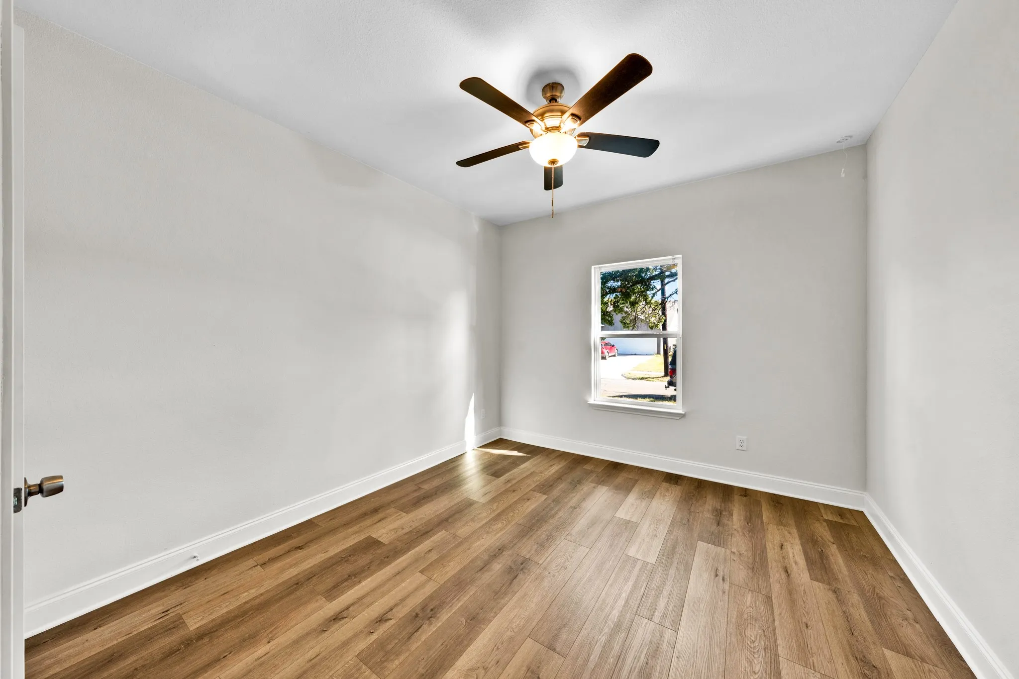 Spacious room featuring wood-finish flooring, a ceiling fan with integrated lighting, and a single window