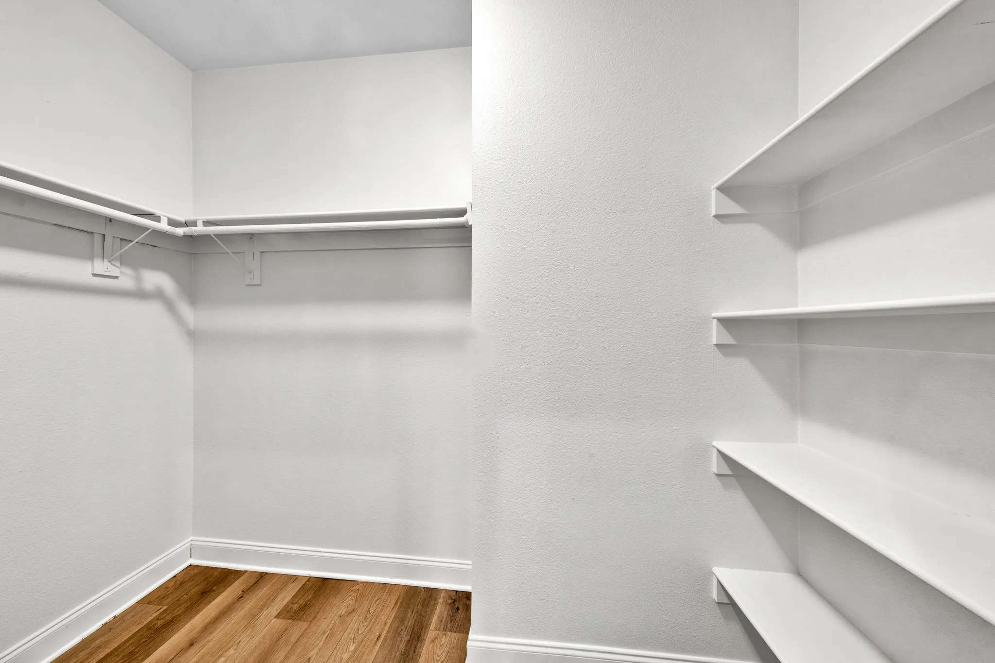Walk-in closet with hanging rods, built-in shelving, white trim, and wood-finish flooring